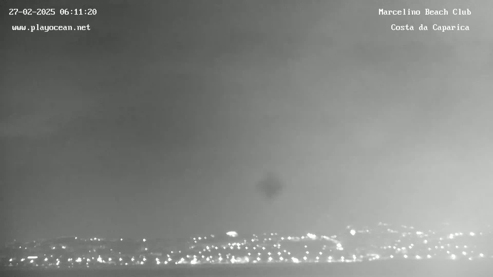 A hazy, overcast sky over a distant city skyline at night, faintly lit by many small lights.