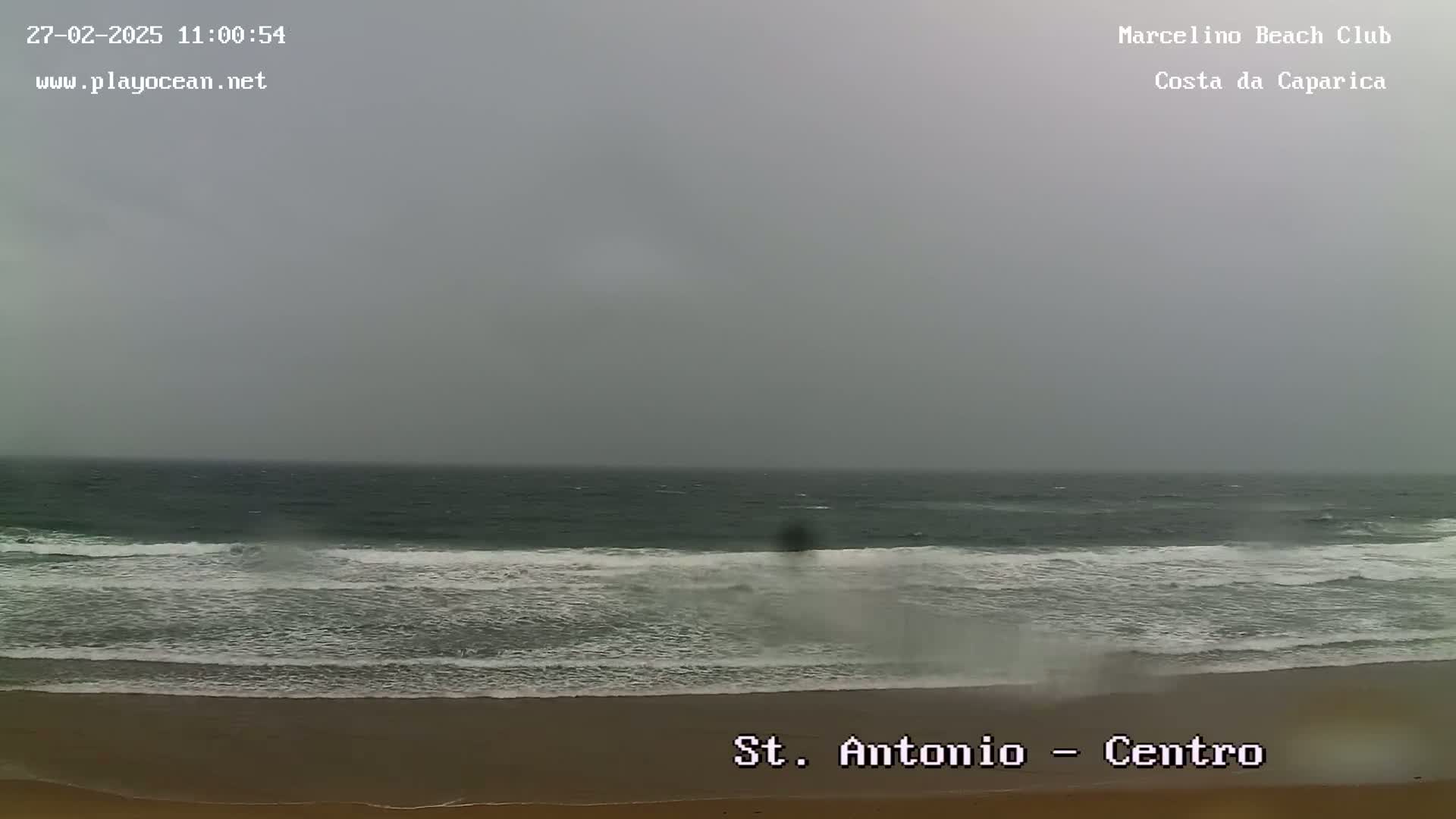 A grey, overcast day shows a sandy beach with waves breaking on the shore.
