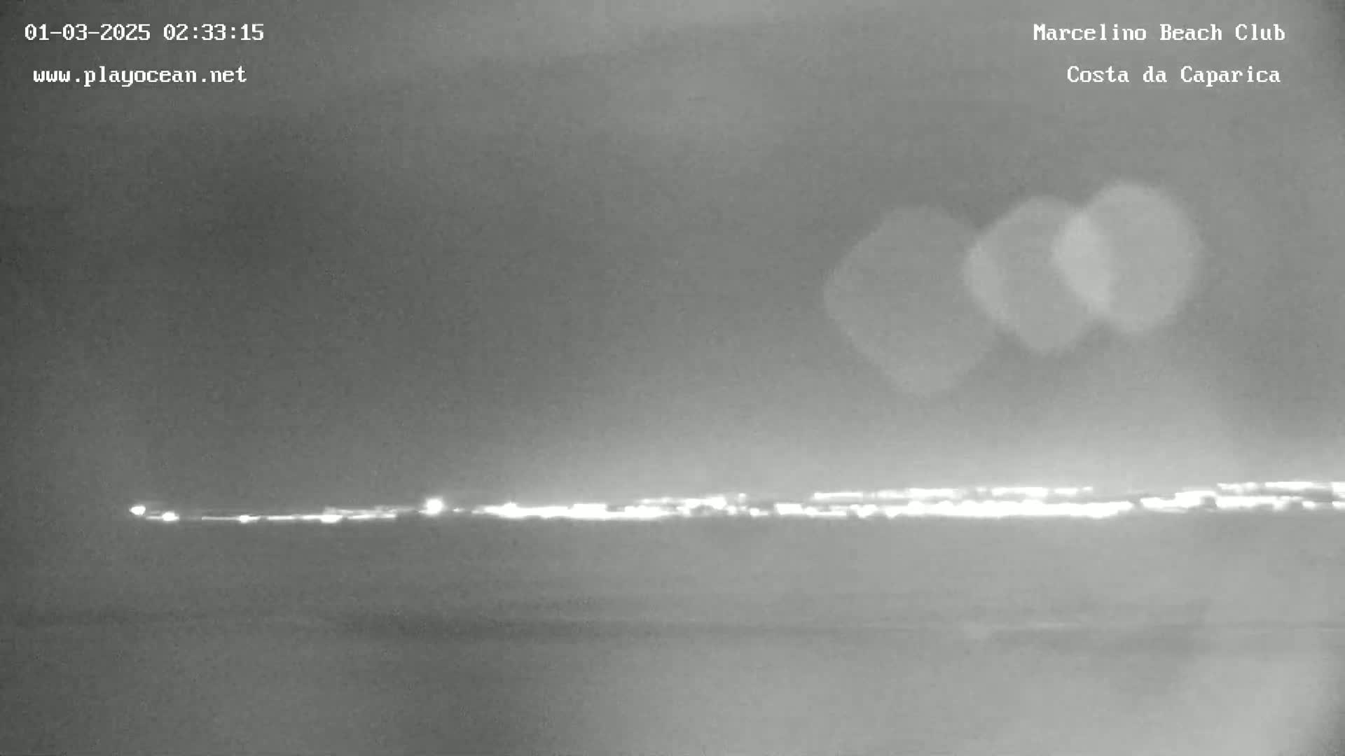 A nighttime, low-light view shows a distant line of lights across a dark horizon.