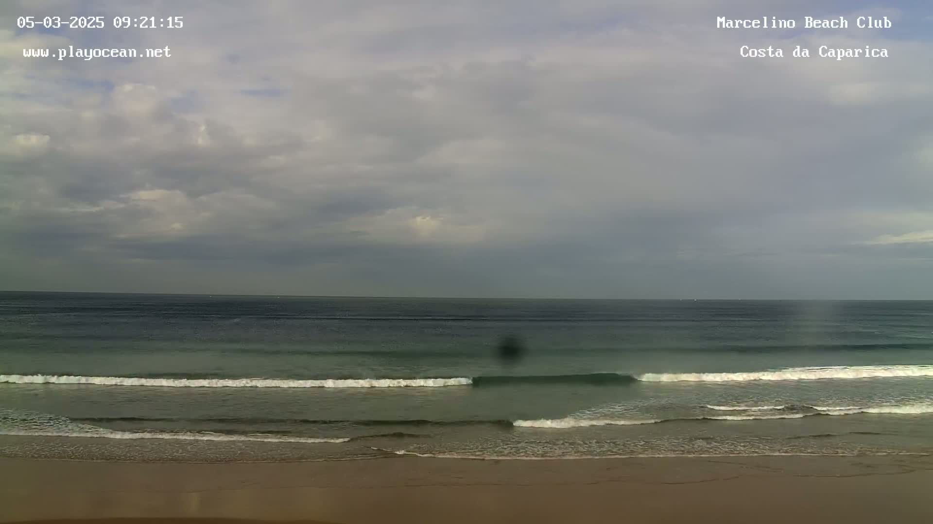 A sandy beach meets a calm ocean under a cloudy sky.