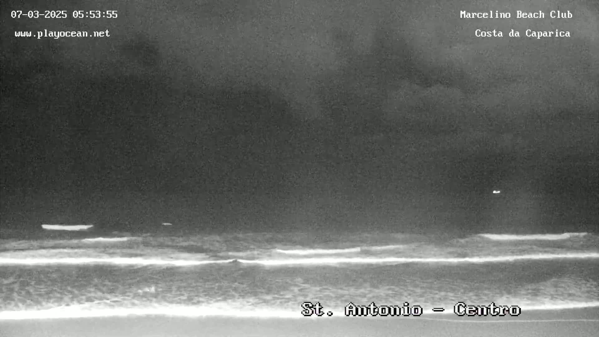 A nighttime beach scene shows dark, cloudy skies over gently lapping waves.
