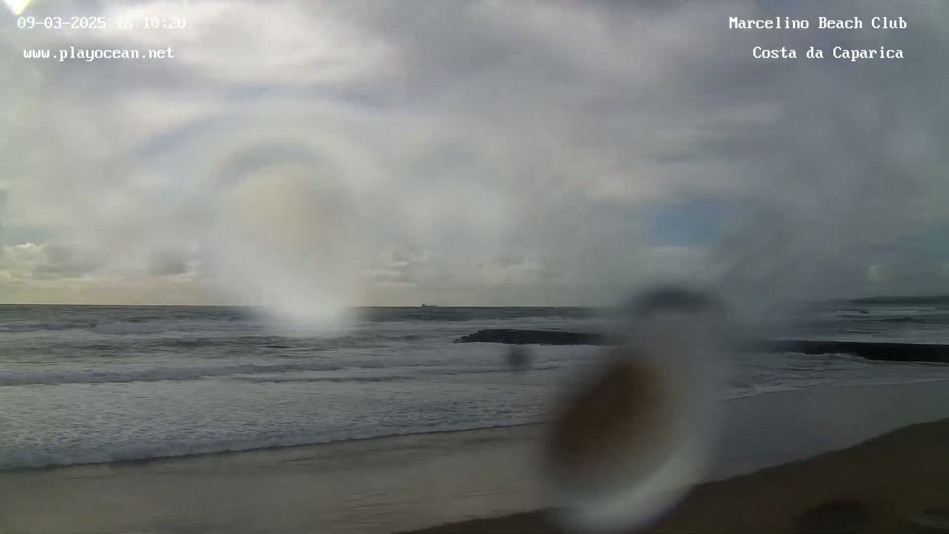 A beach scene is shown with overcast skies and waves rolling onto the shore.