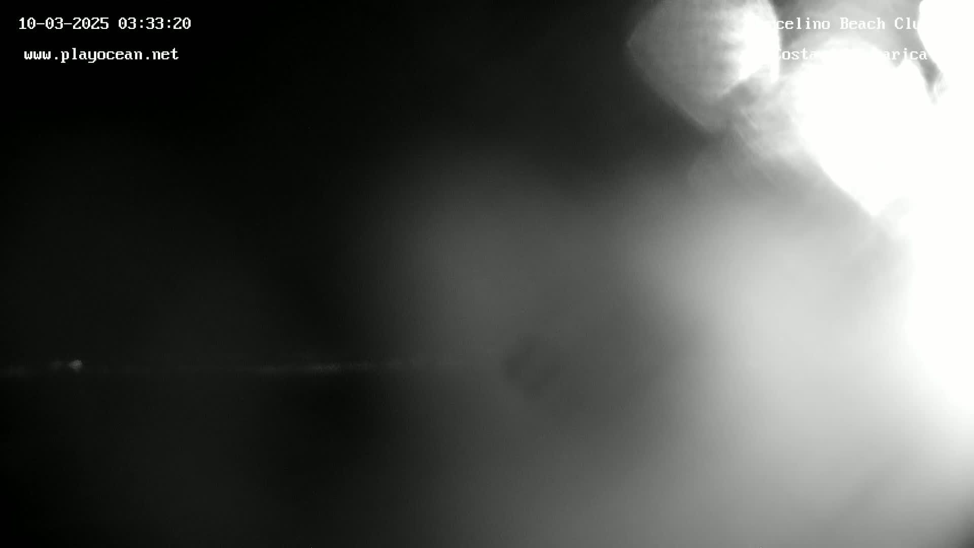 A blurry, dark grayscale image shows a bright area in the upper right corner against a dark background, possibly at night.