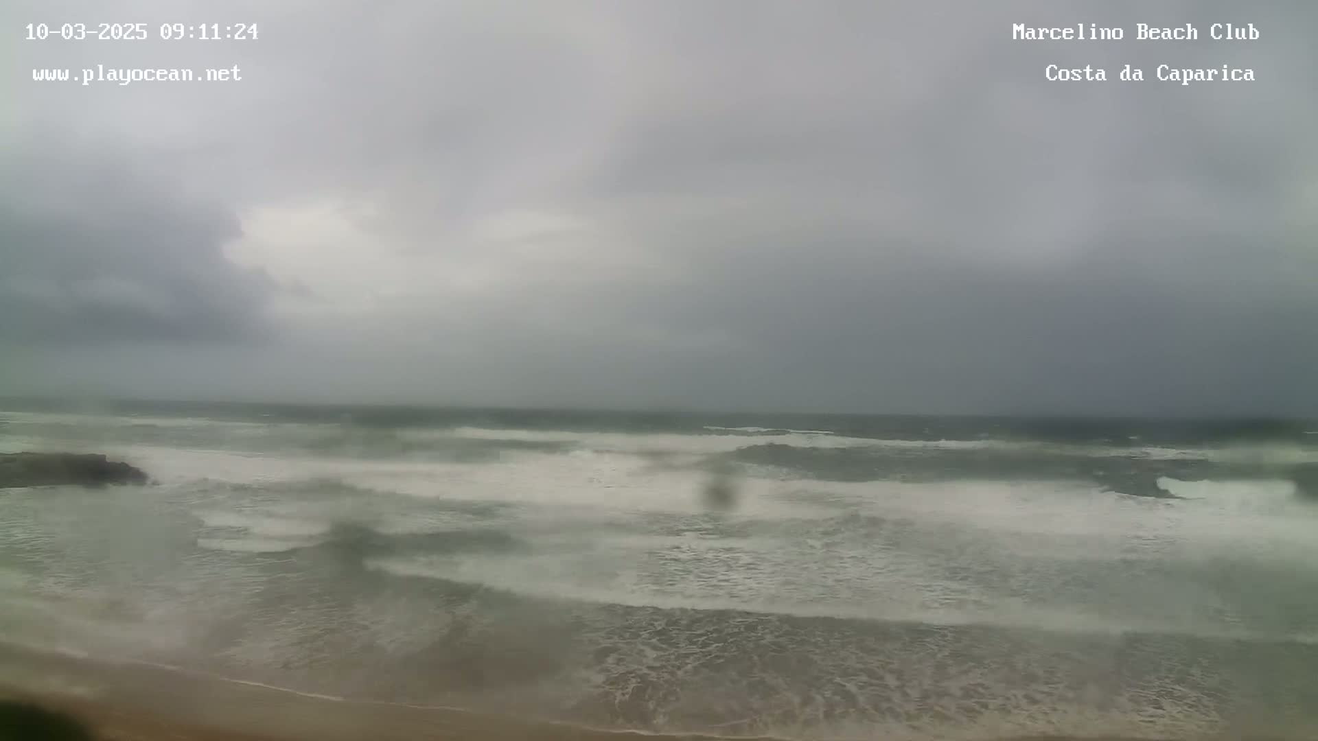 A beach with choppy, grey-white waves under an overcast sky.