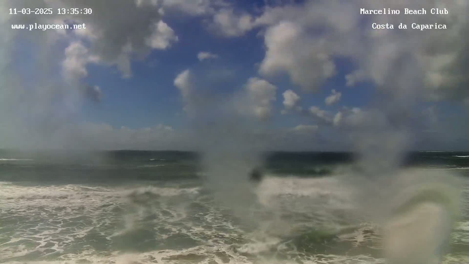 A partly cloudy day shows rough ocean waves crashing on a beach.