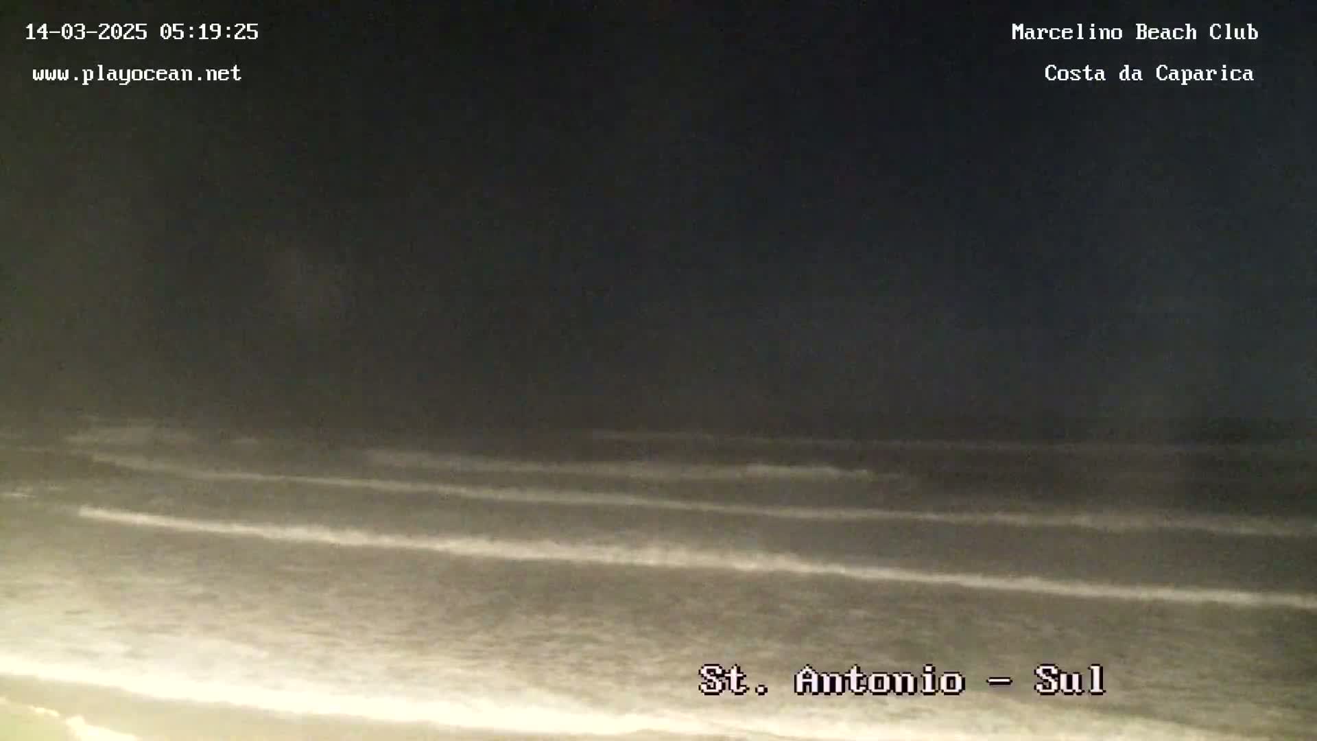 A nighttime view of gently rolling waves on a dark ocean beach under a dark sky.