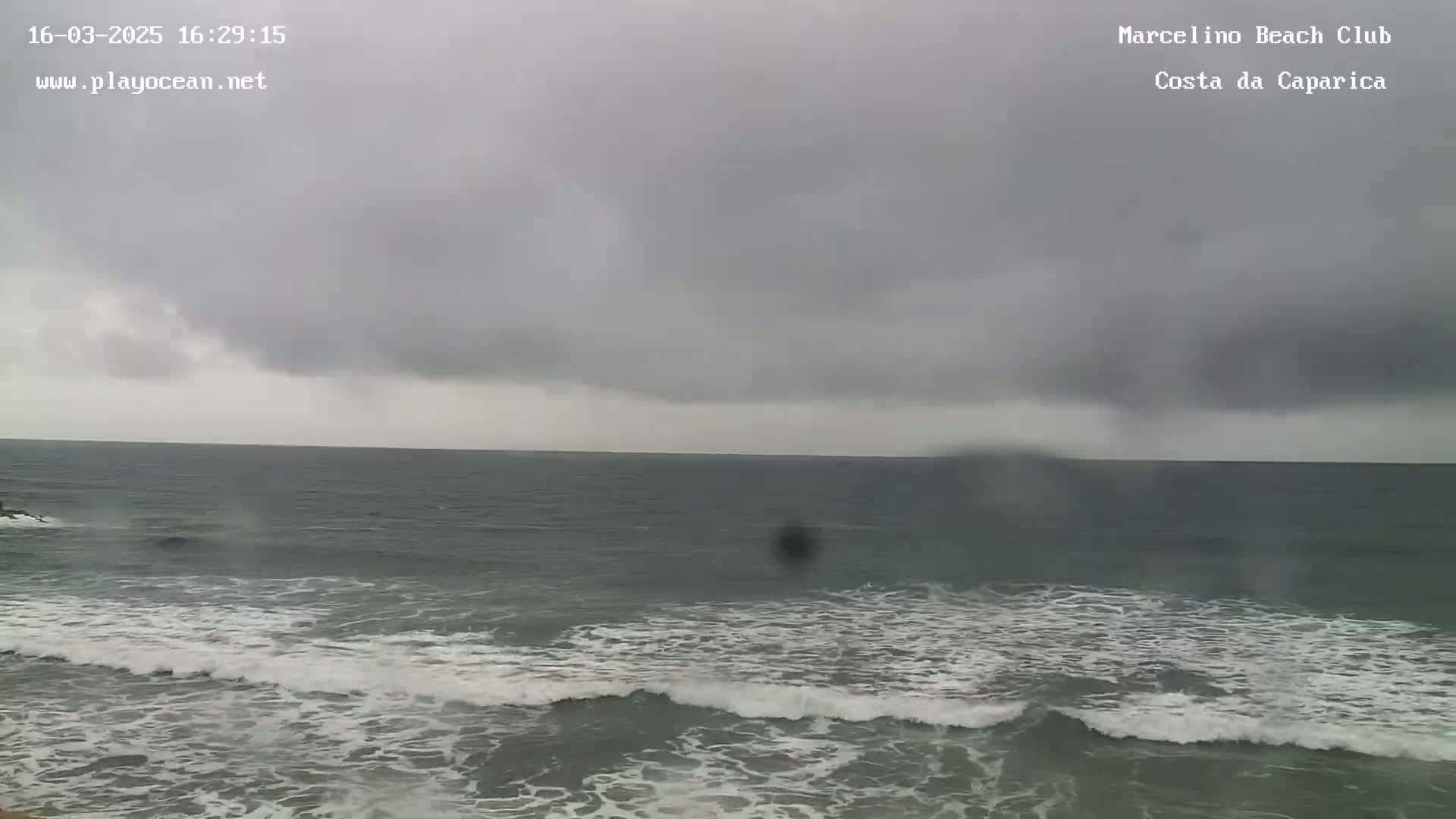 A dark, overcast sky hangs over a gray ocean with small waves breaking on the shore.