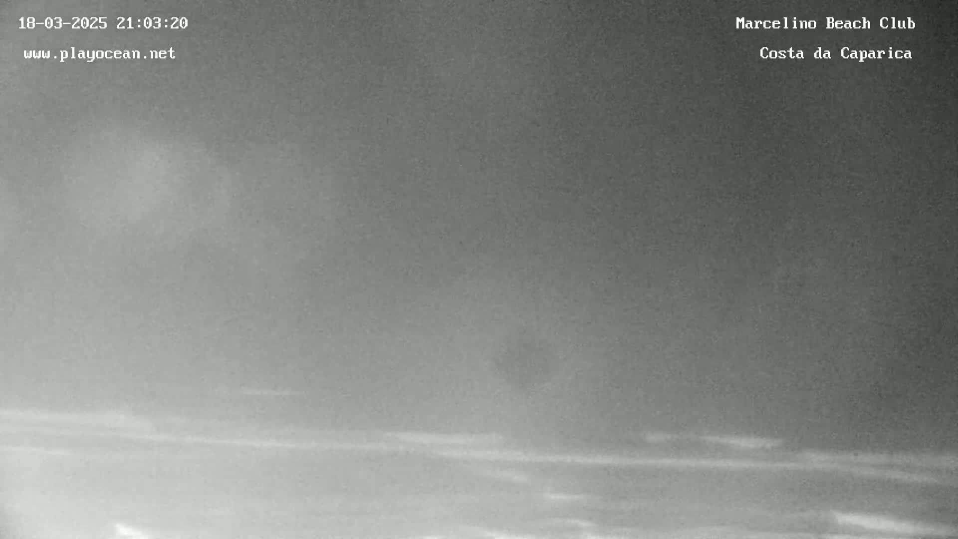 A nighttime, hazy view of a beach, possibly with some very faint waves visible.