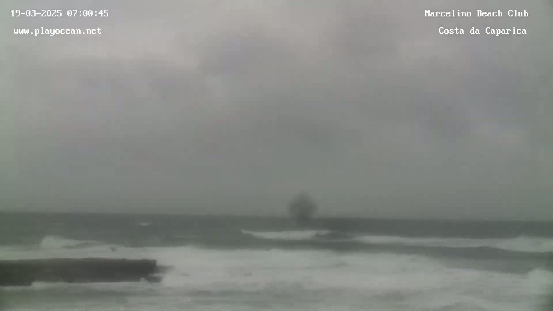 A gray, overcast day shows a choppy ocean with waves breaking near a dark shoreline.