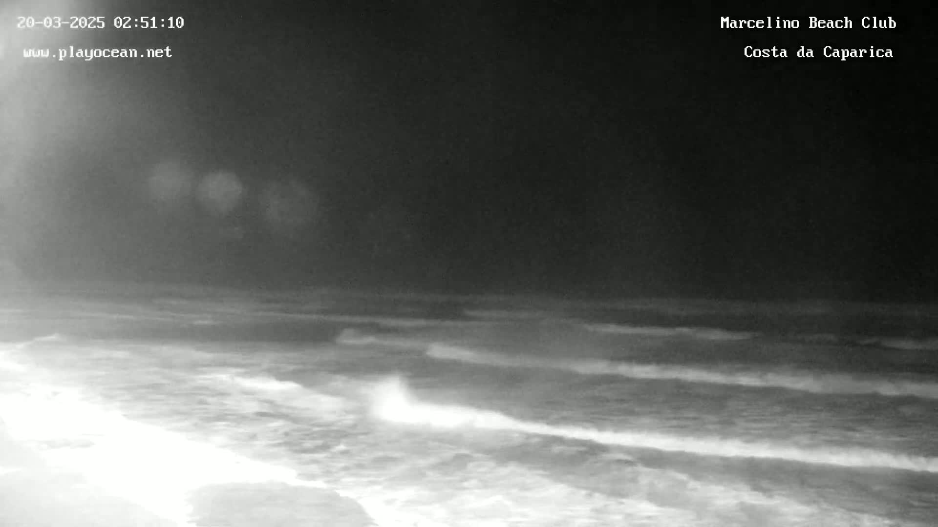 A nighttime view of ocean waves breaking on a beach under a dark sky.
