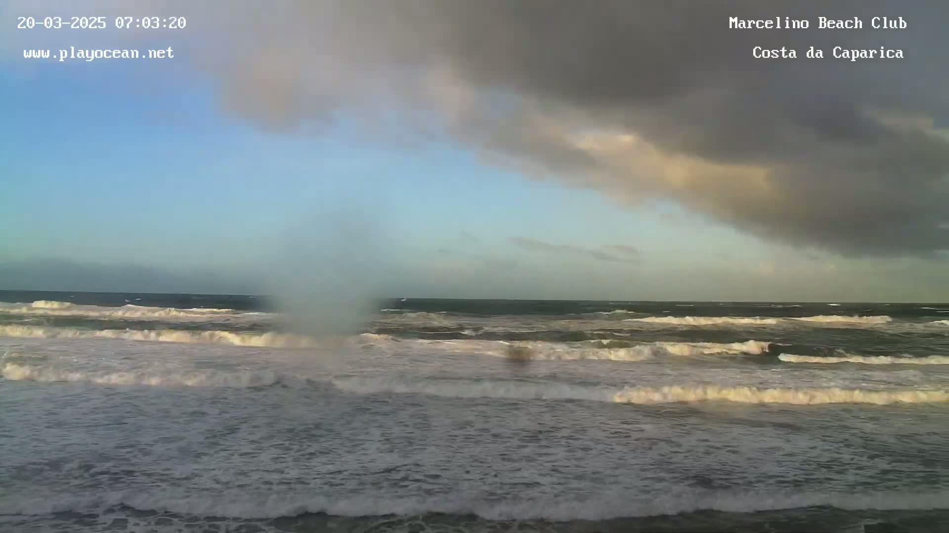 A dark, cloudy sky hangs over a choppy ocean with waves breaking onto a shore.