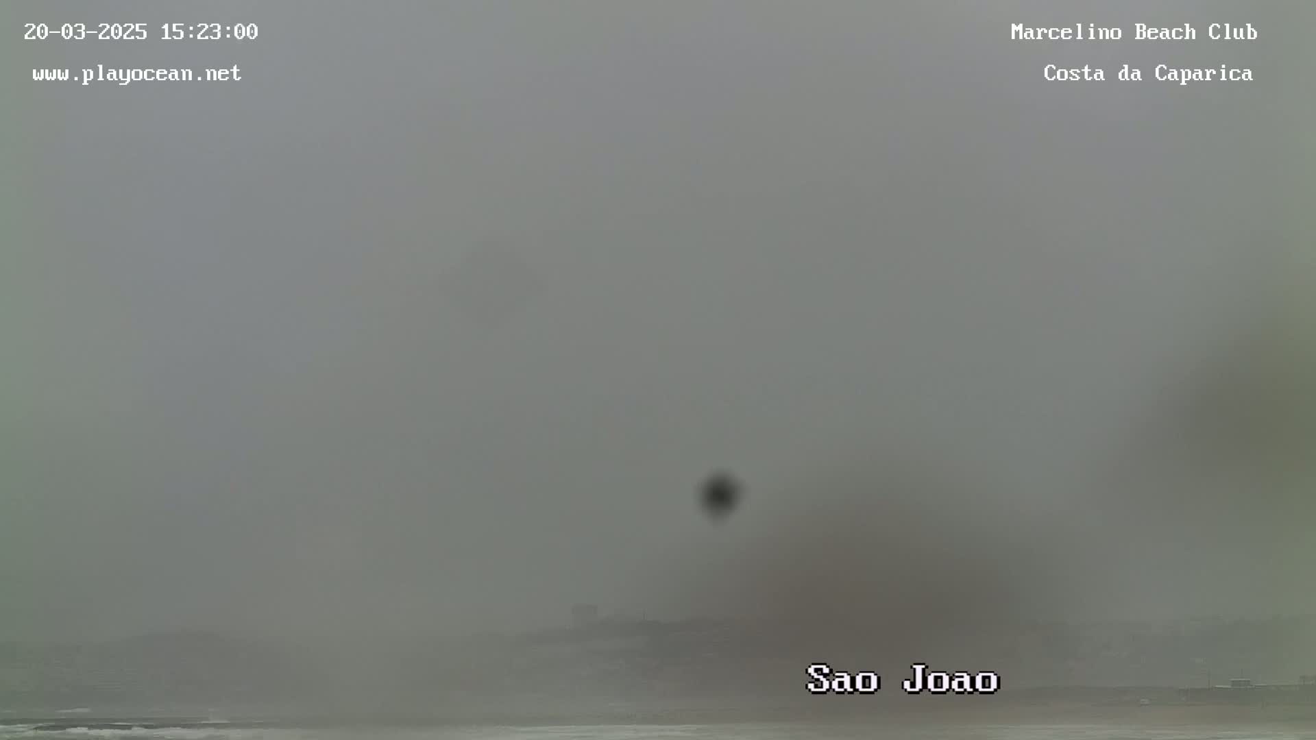 A hazy, overcast view of a beach and ocean, with a distant shoreline barely visible.