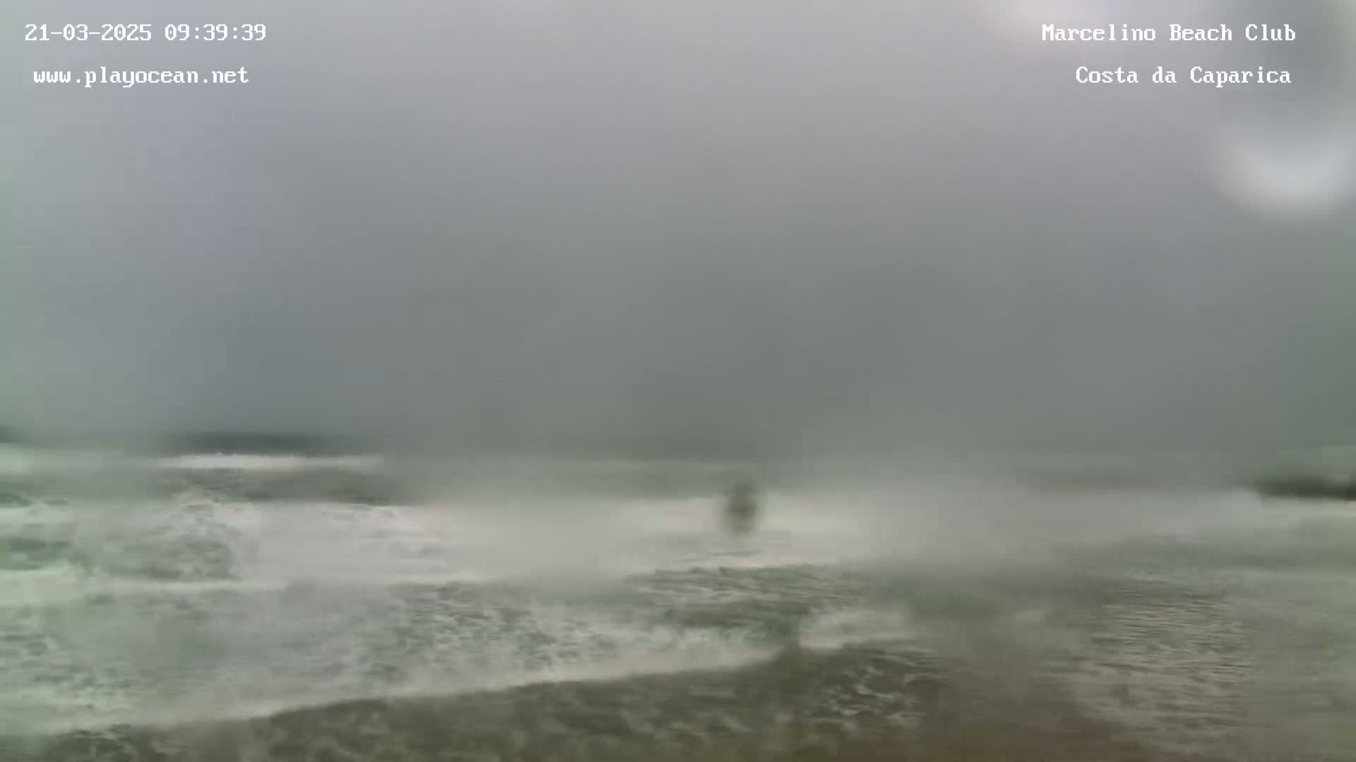 A hazy, overcast day shows turbulent ocean waves crashing on a beach.