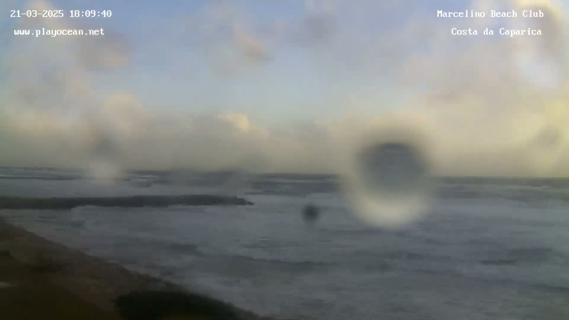 A blurry, overcast view of a turbulent ocean seen from a coastal vantage point, with rain obscuring the view.