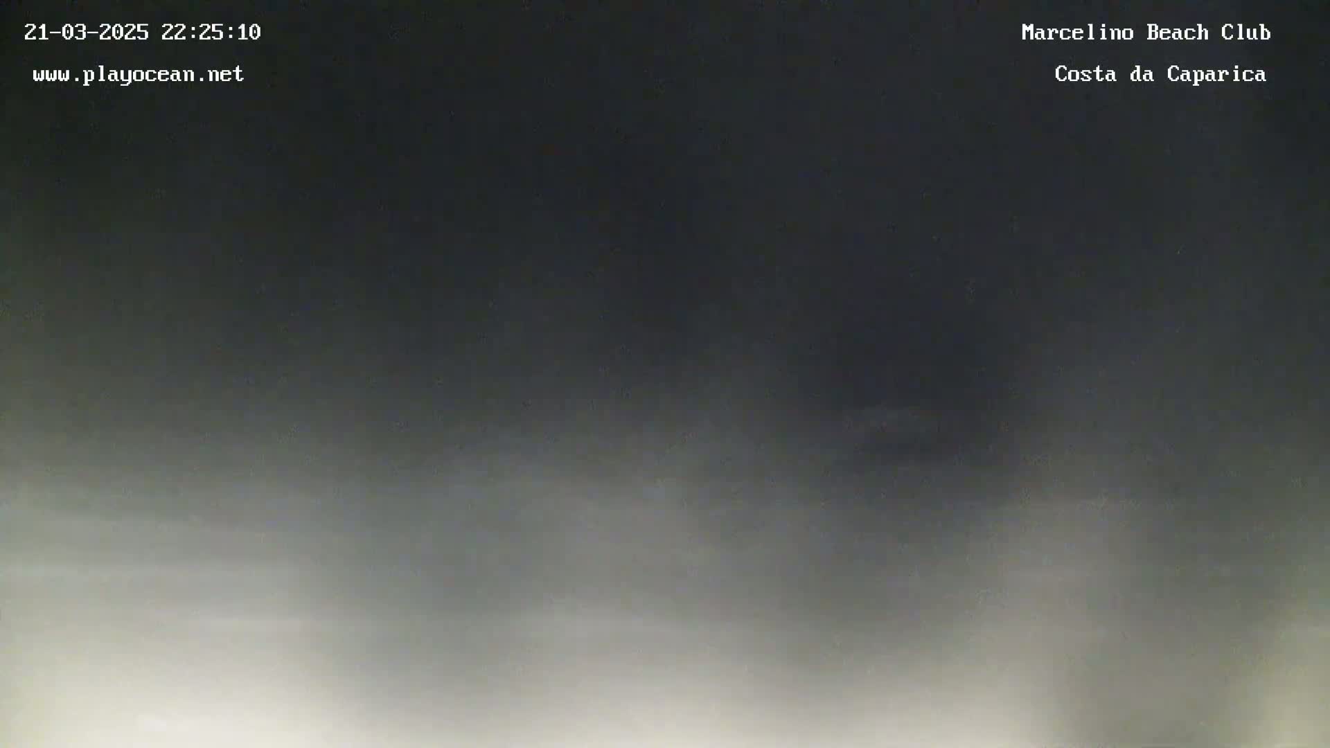 A nighttime, hazy view of a beach, possibly showing fog or low clouds near the horizon.