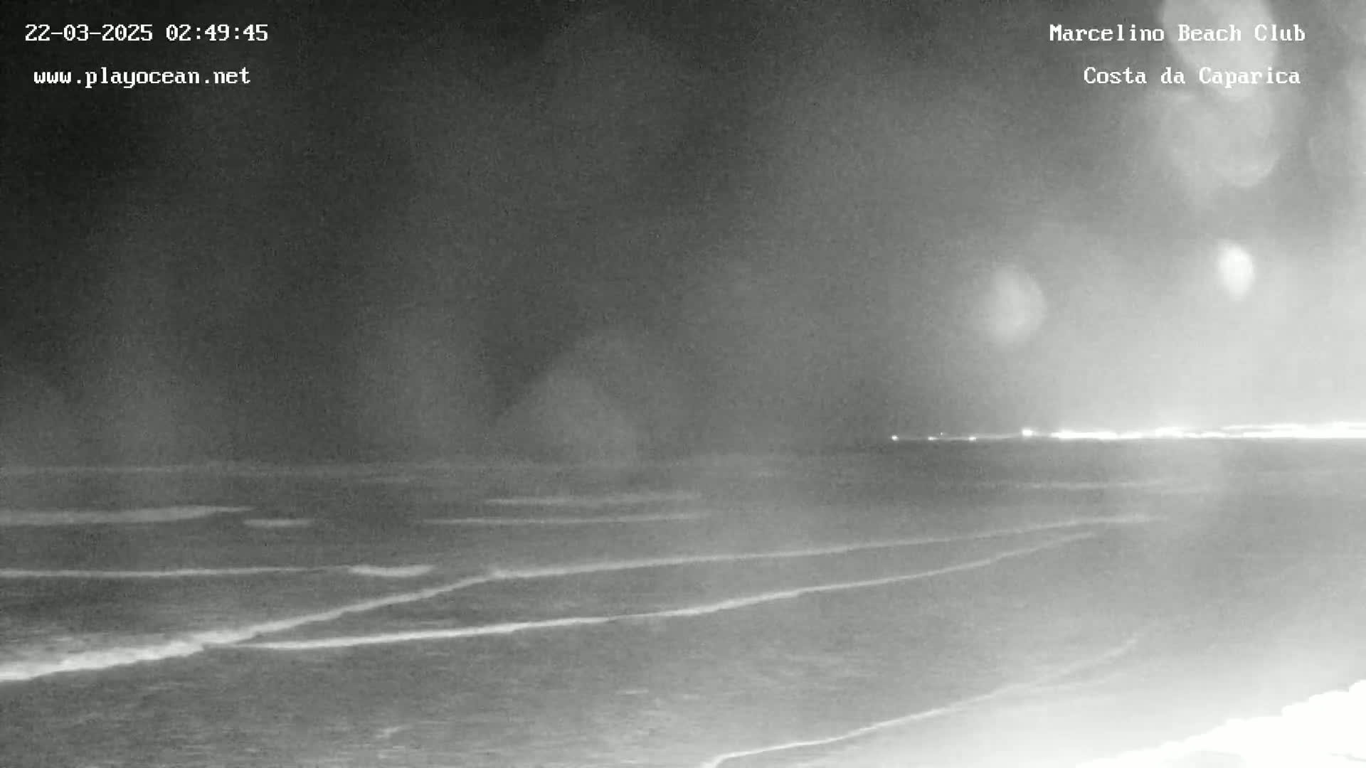 A nighttime, low-light view of gently rolling waves on a dark ocean beach.