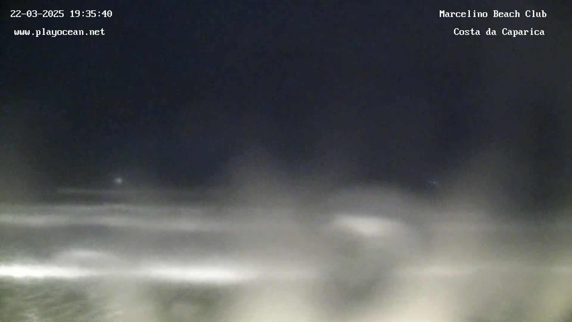 A nighttime view of a beach with hazy or foggy conditions, showing dark skies and indistinct waves.