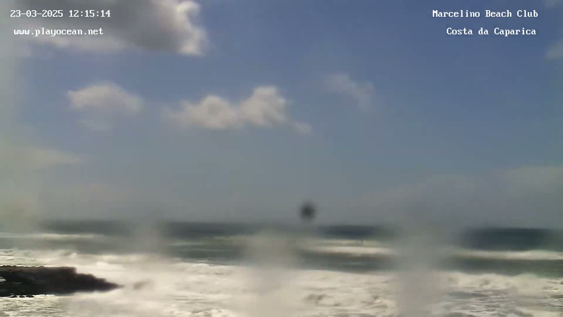 A partly cloudy sky overlooks a rocky shoreline with choppy waves crashing against it.