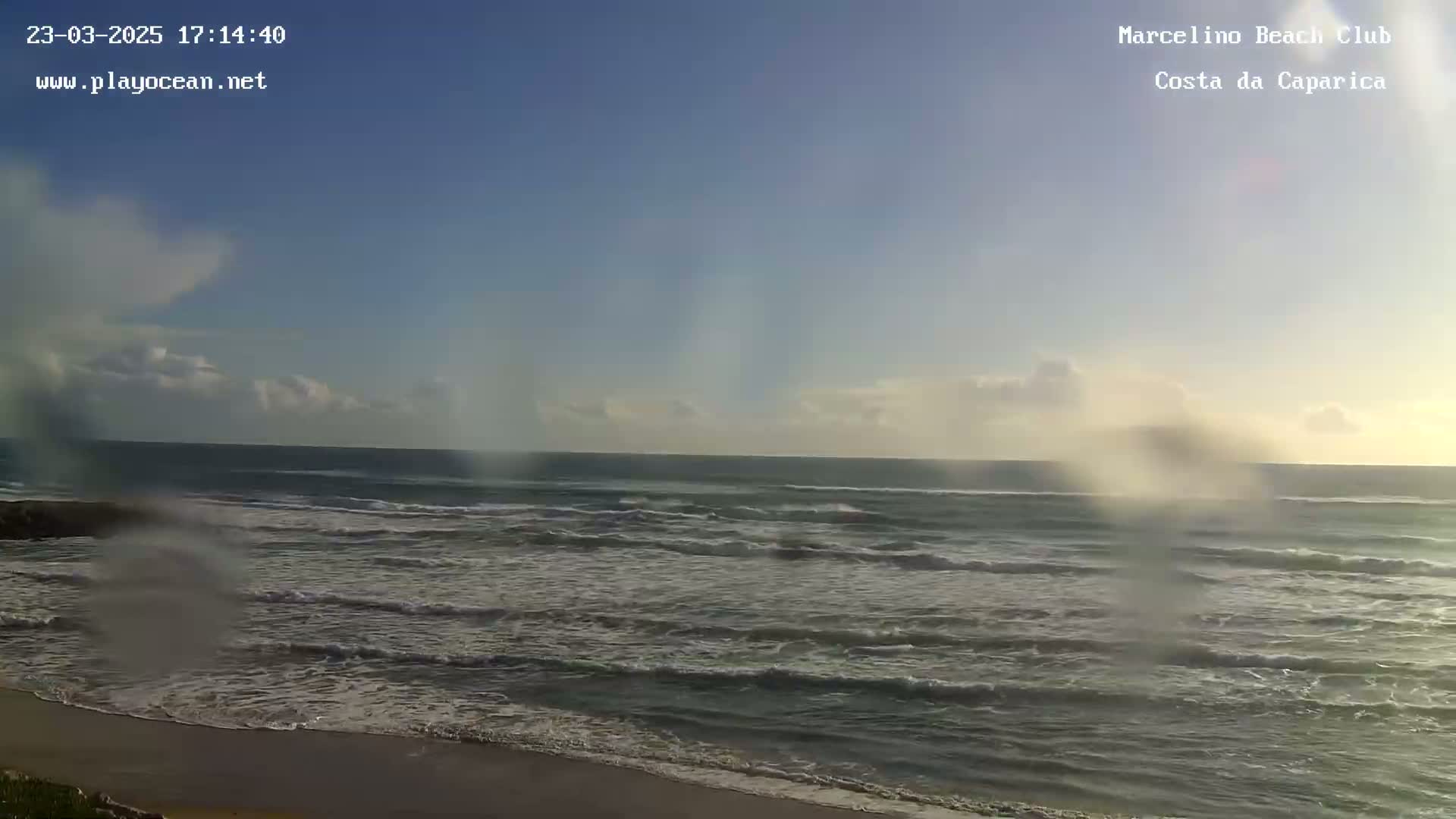 A mostly sunny day shows a beach with gentle waves rolling onto the shore.