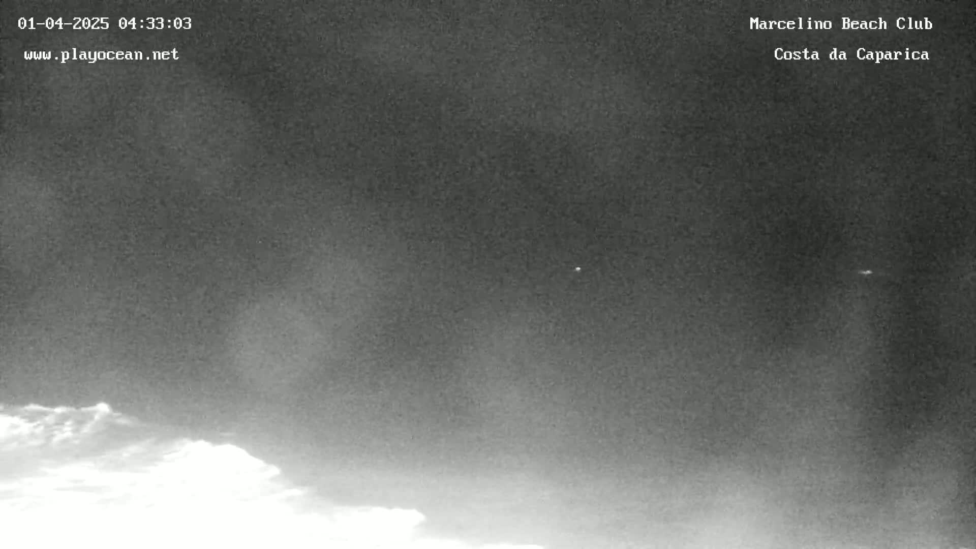 A low-light nighttime image shows a dark sky with a few small, bright lights and some low clouds at the bottom of the frame.