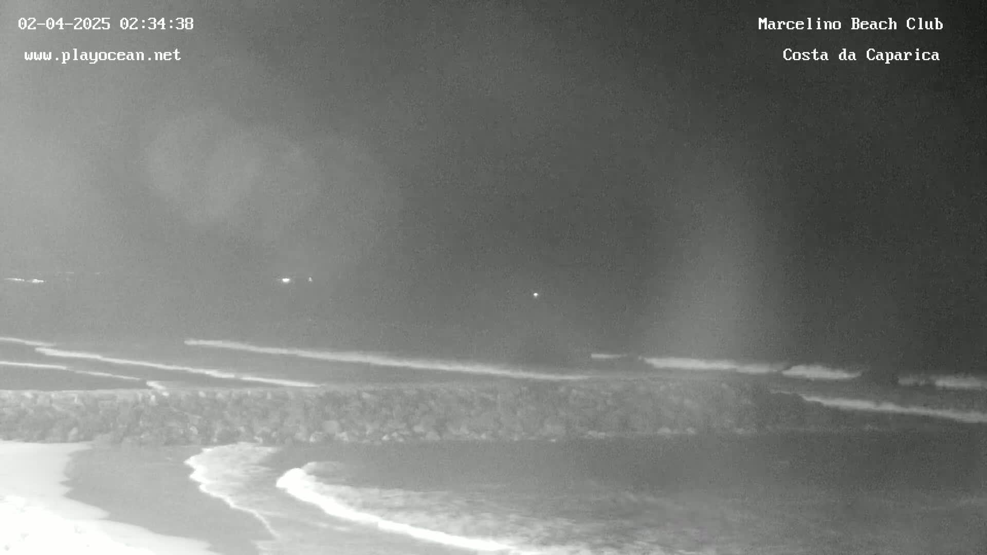 A nighttime, low-light view of a beach with gentle waves lapping against a rocky barrier.