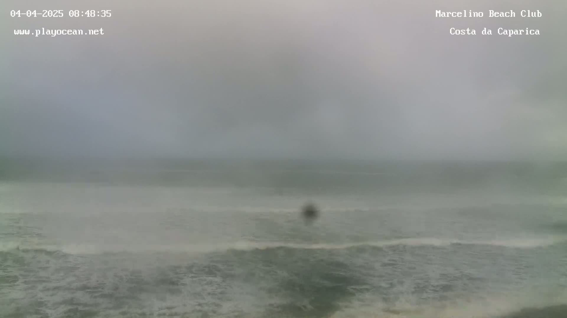 A hazy, overcast day shows a choppy ocean with small waves breaking on the shore.