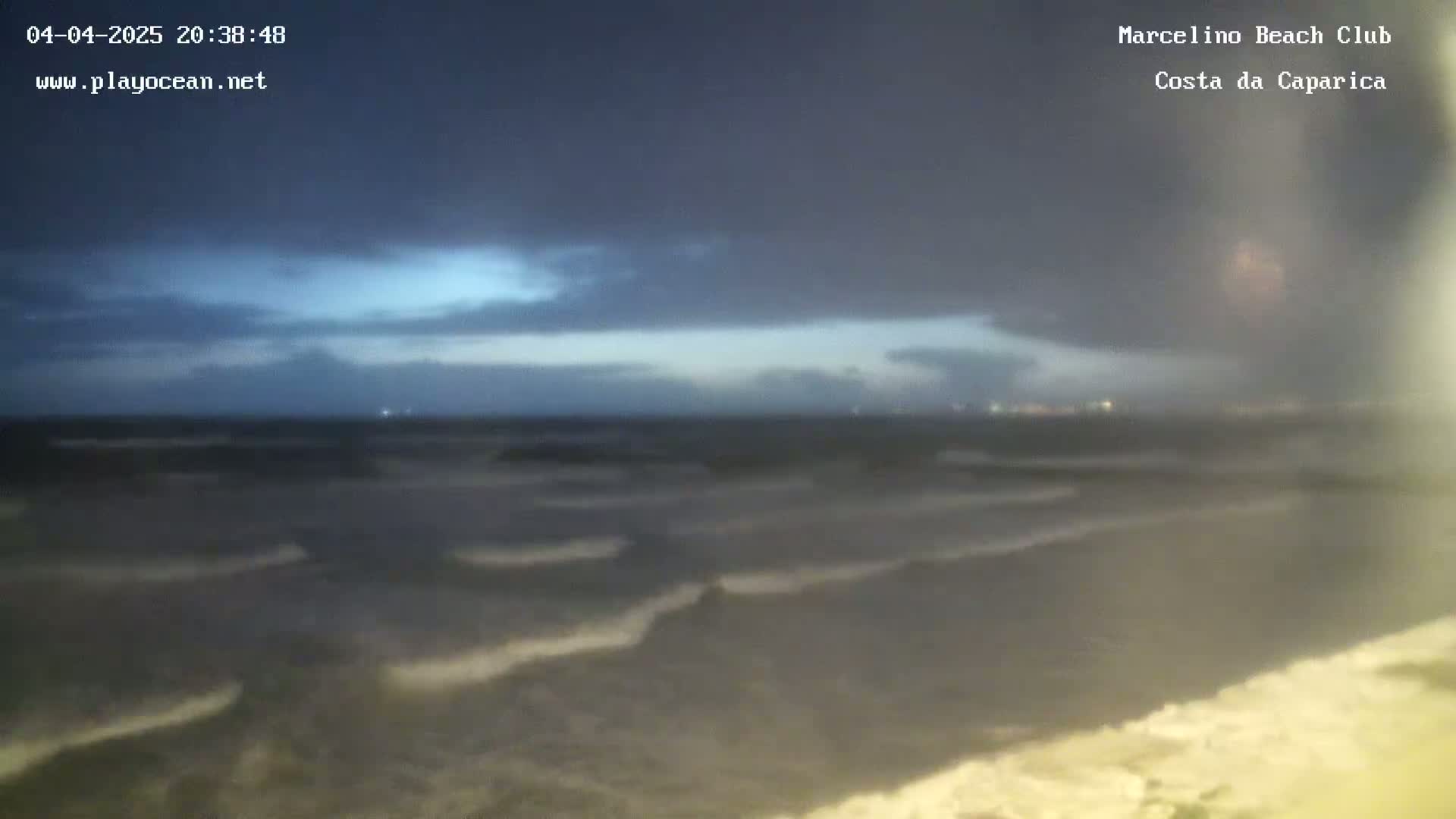 Under a dark, cloudy sky, waves roll onto a beach at night.