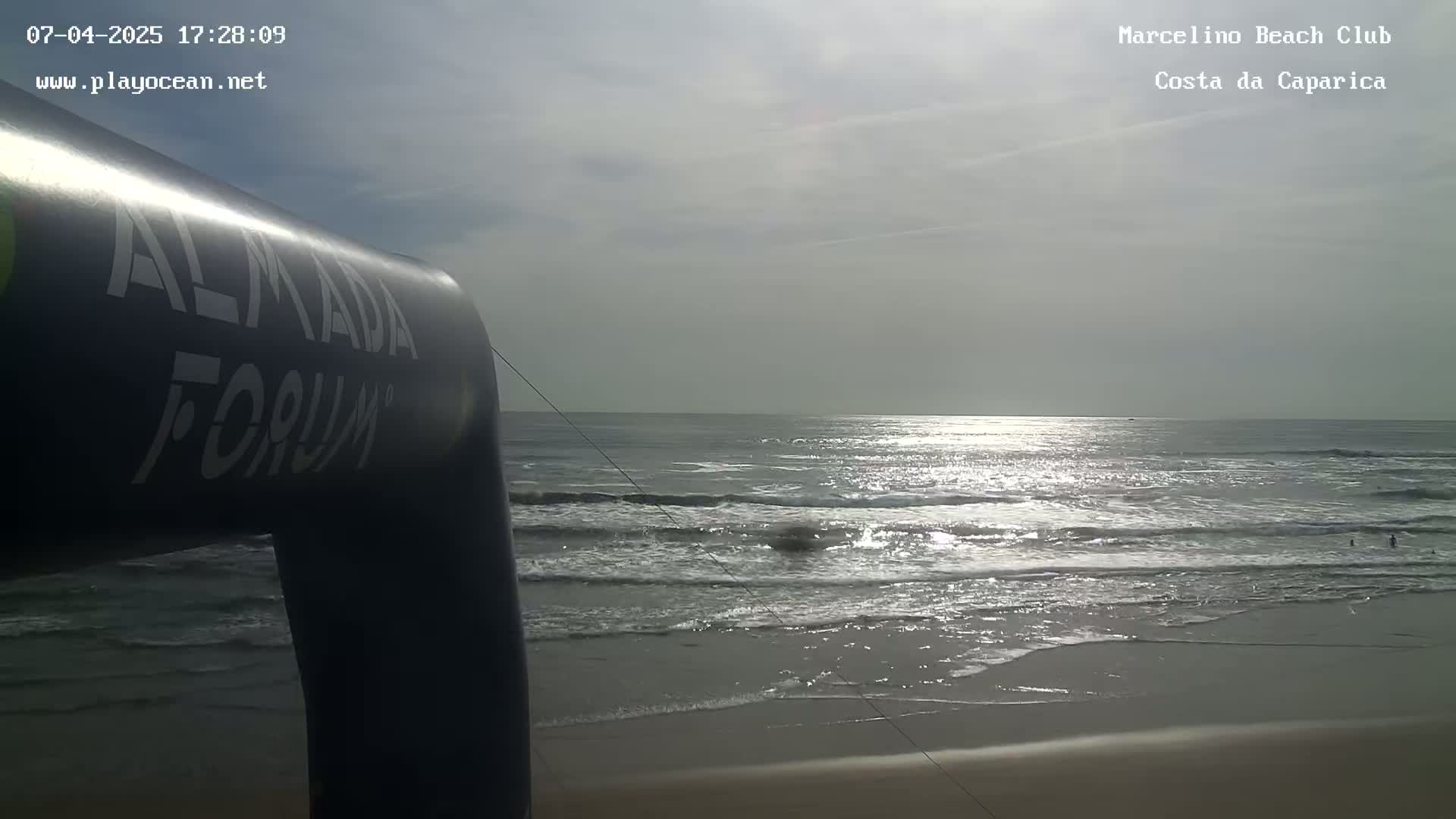 A partly cloudy day at a beach shows gently rolling waves lapping at the shore near an inflatable arch.
