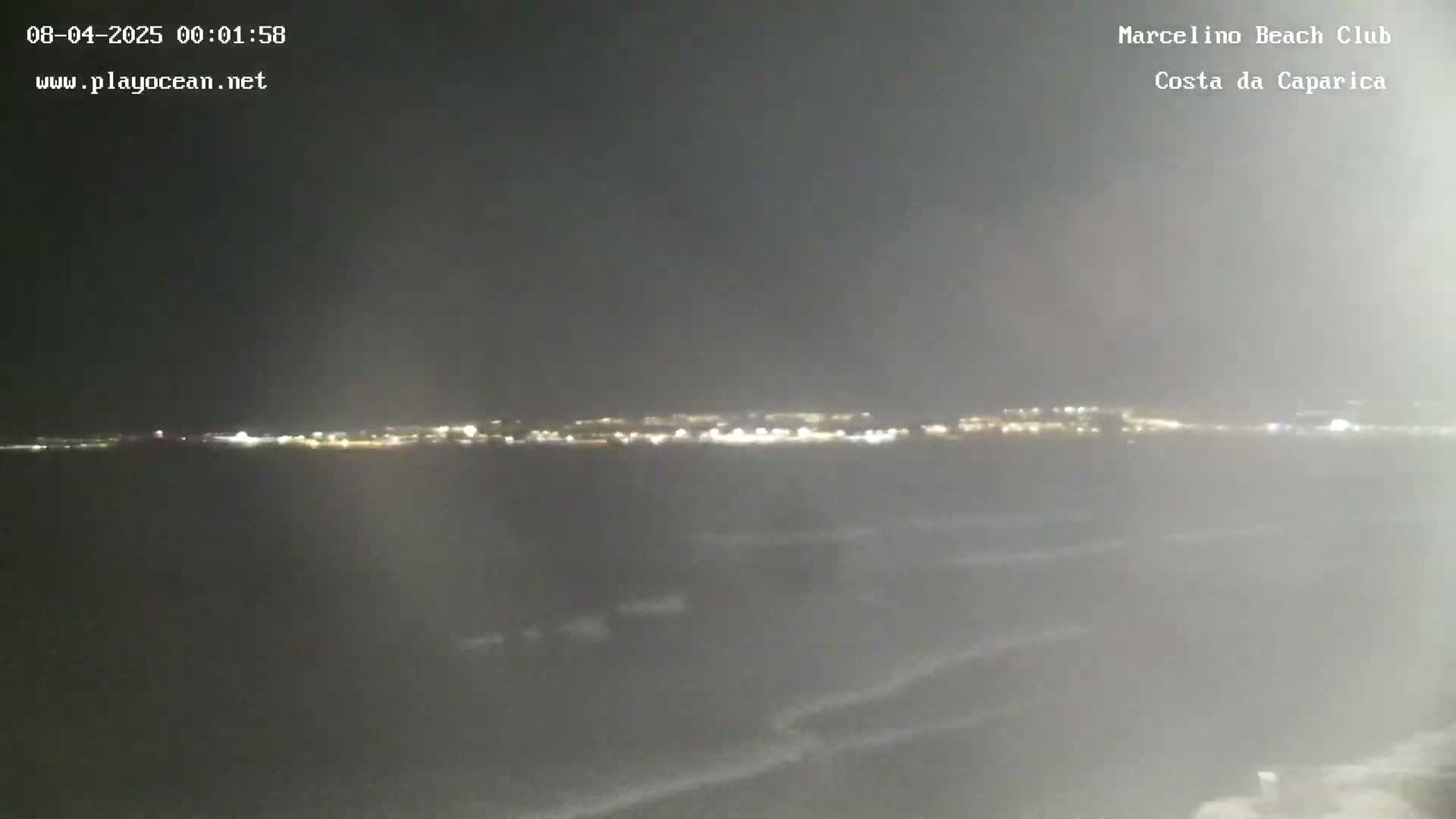 A nighttime view of a city's lights across a dark body of water with slight wave action.