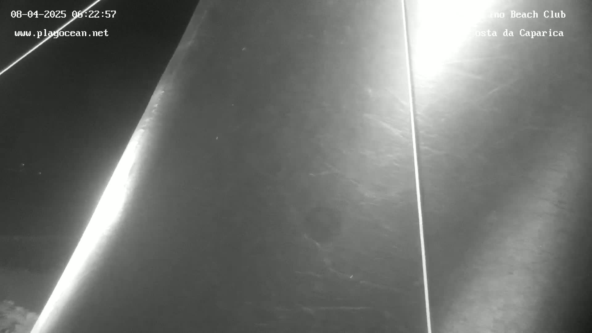 A nighttime, low-light image shows a dark, textured surface, possibly water, with two vertical lines and a brighter area suggesting light reflection.