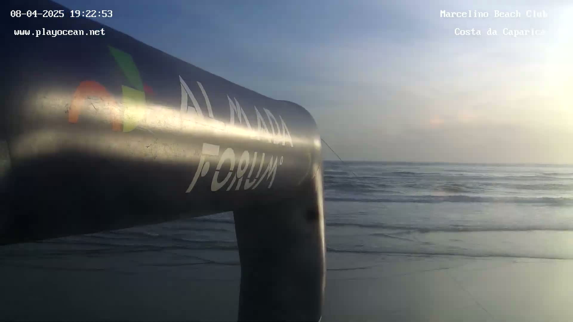 A large inflatable arch stands on a sandy beach overlooking a calm ocean under a clear, twilight sky.