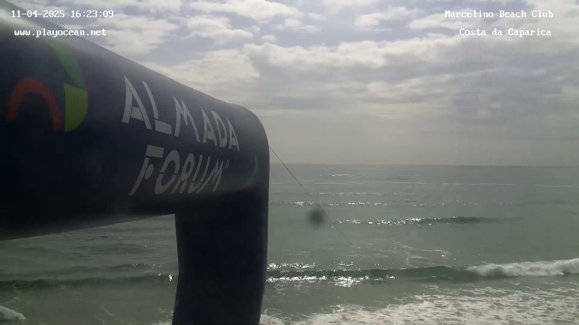 A dark-blue inflatable structure partially obscures a view of a calm ocean with small waves under a cloudy sky.