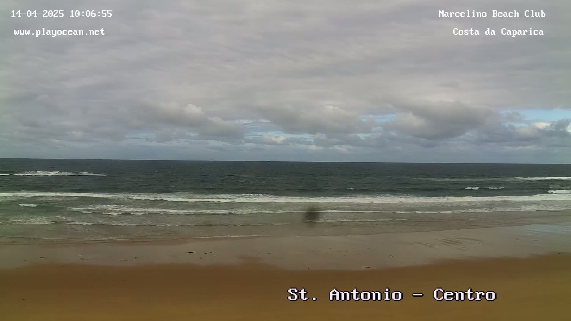 A sandy beach with gentle waves under a cloudy sky.