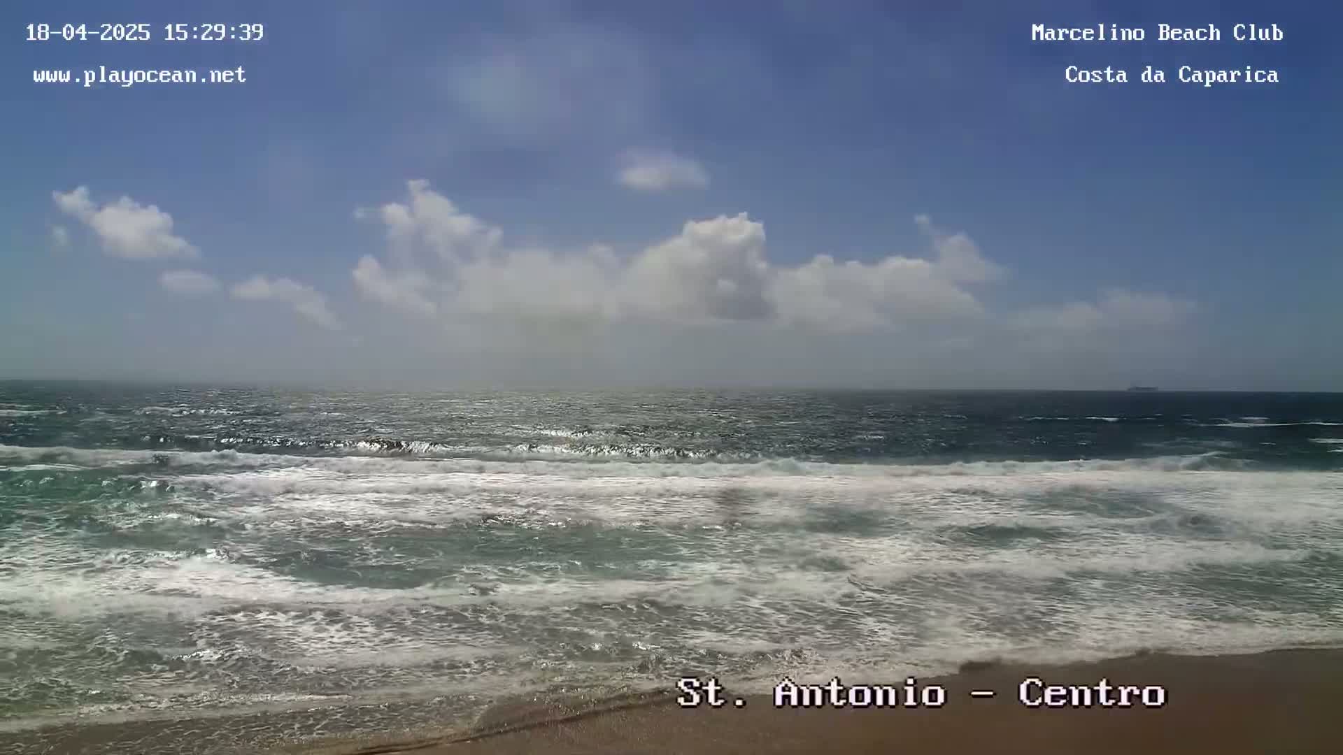 A partly cloudy day shows a sandy beach with moderately sized waves rolling onto the shore.