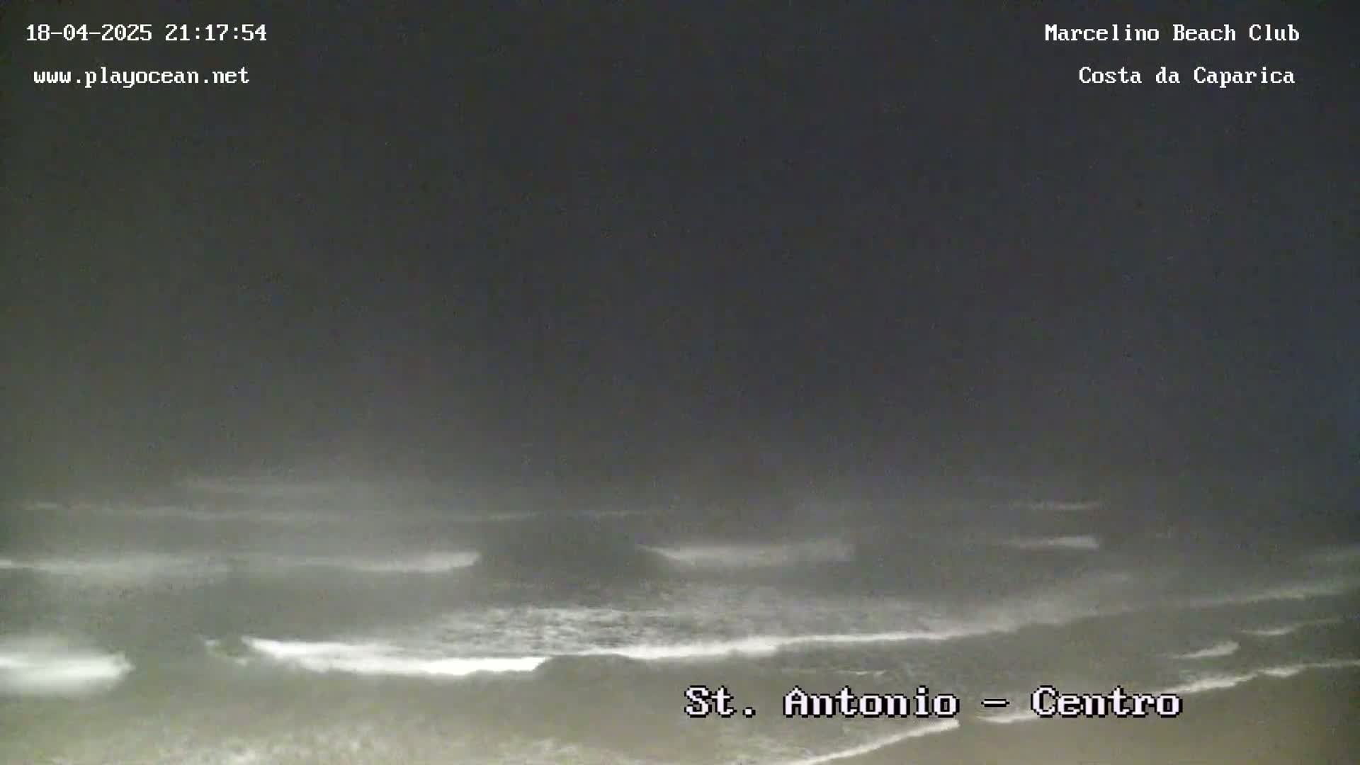 A nighttime view of a beach with dark, choppy waves under a gray, overcast sky.