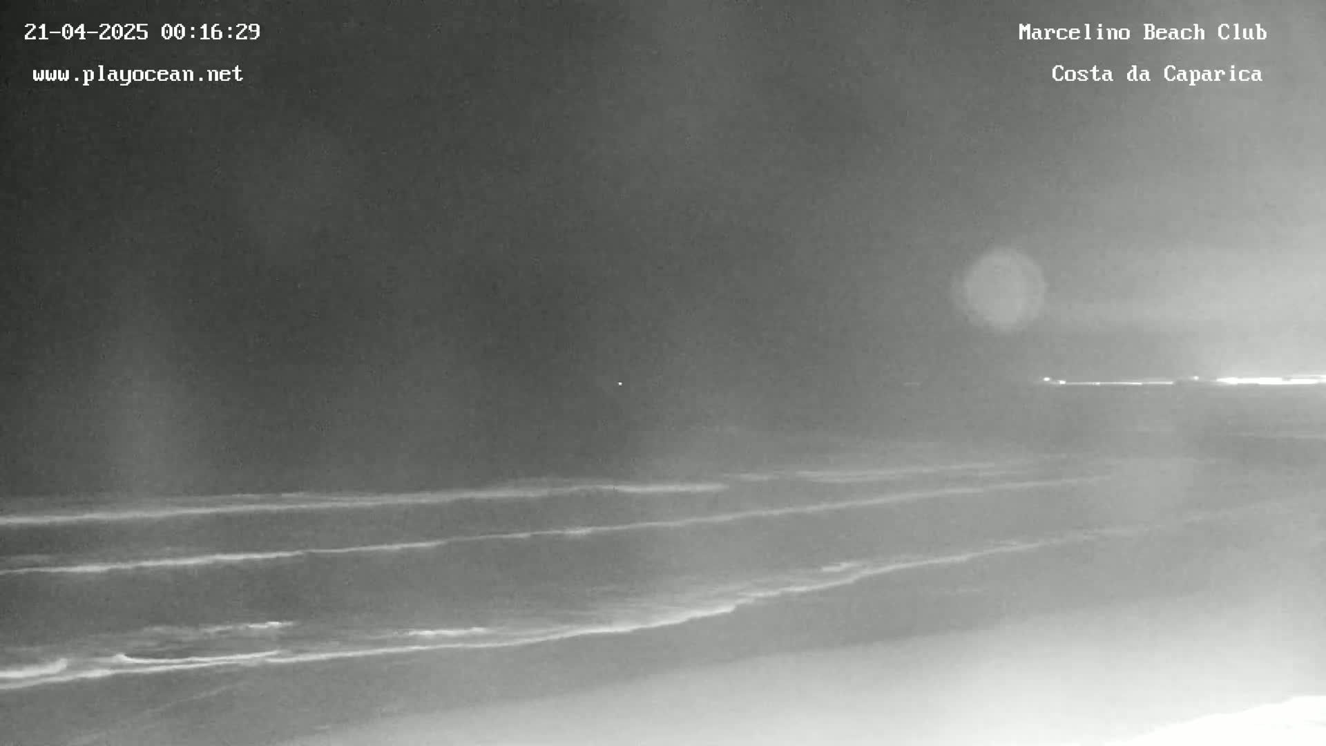 A nighttime, low-light view of a beach with gently rolling waves under a dark sky.
