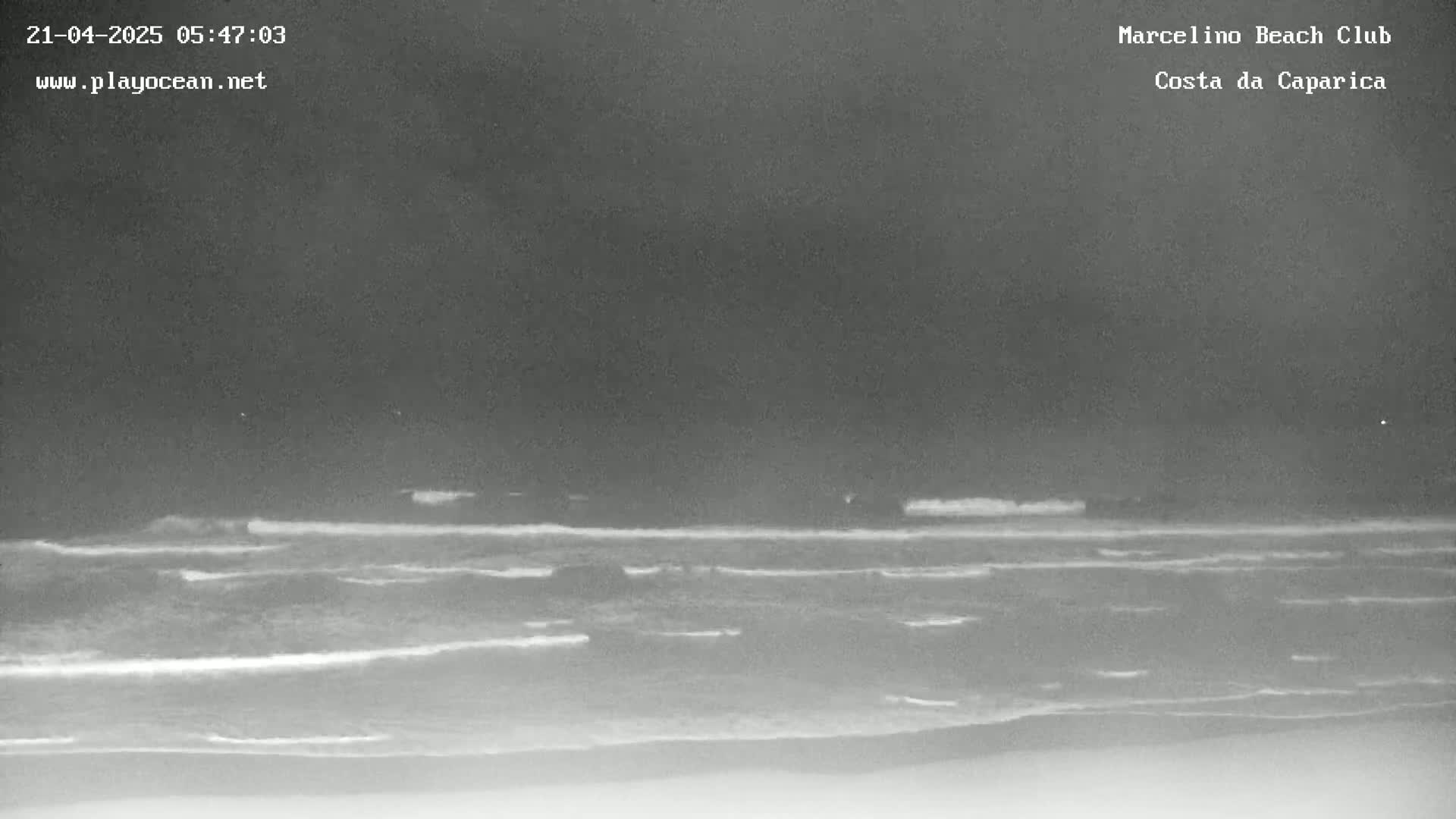 A nighttime, grayscale view of a beach with dark, somewhat choppy waves rolling onto the shore under a dark sky.