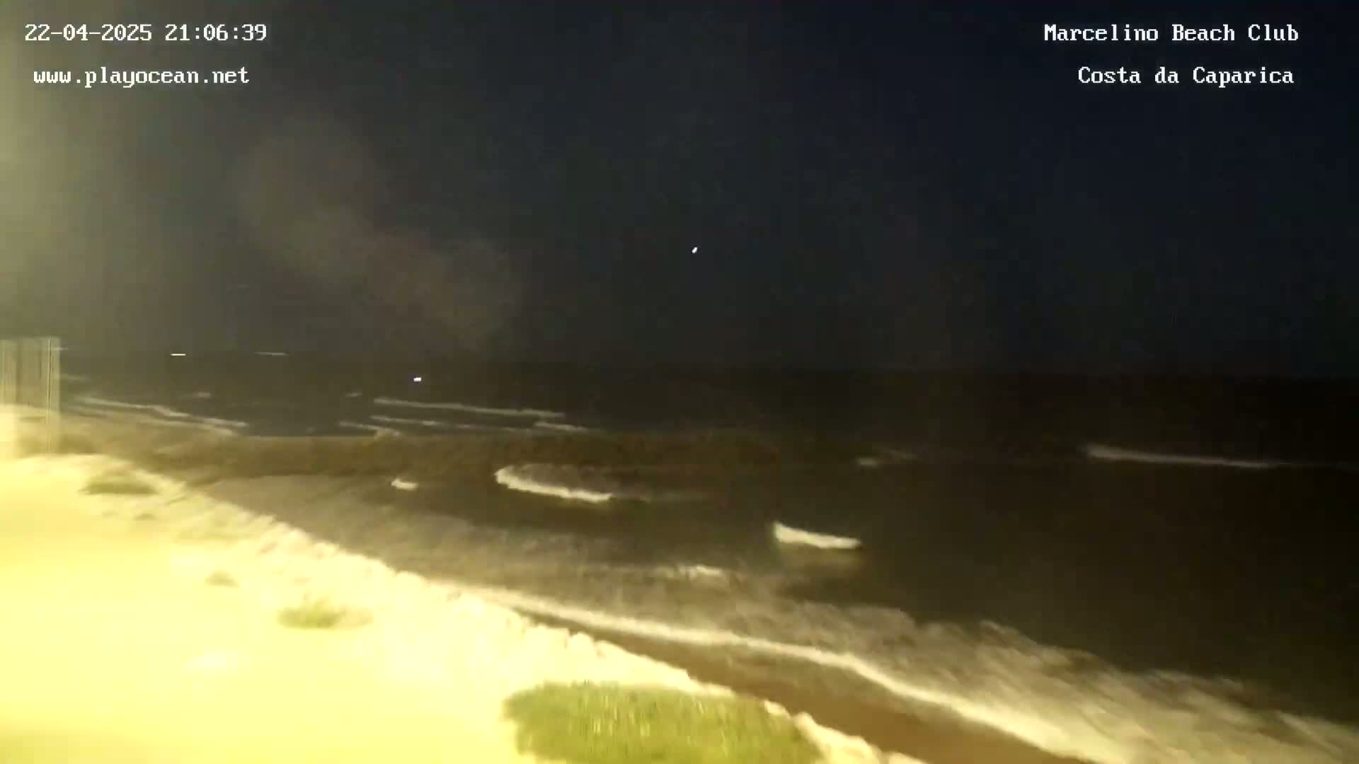 A dark, nighttime view of a beach with gently rolling waves under a clear sky.