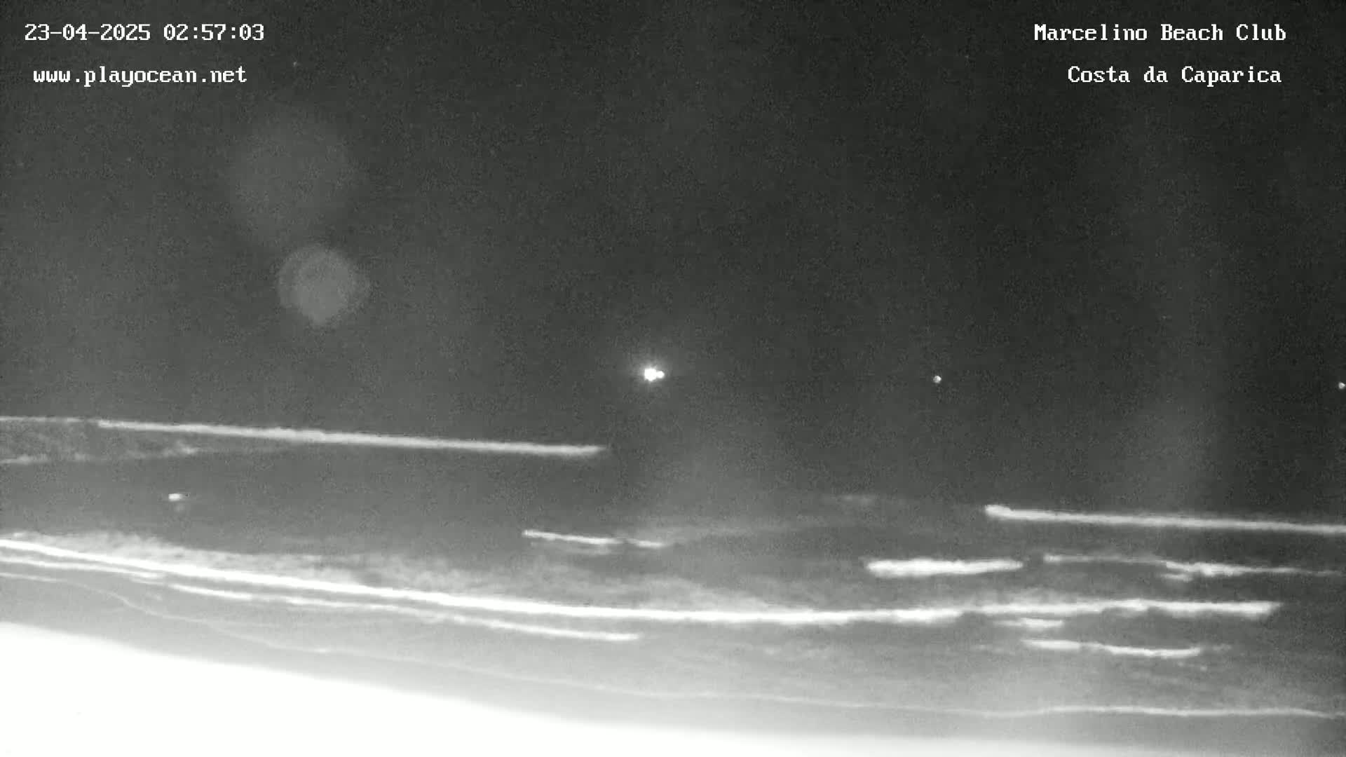 A nighttime view of a dark beach with gently lapping waves under a clear sky.
