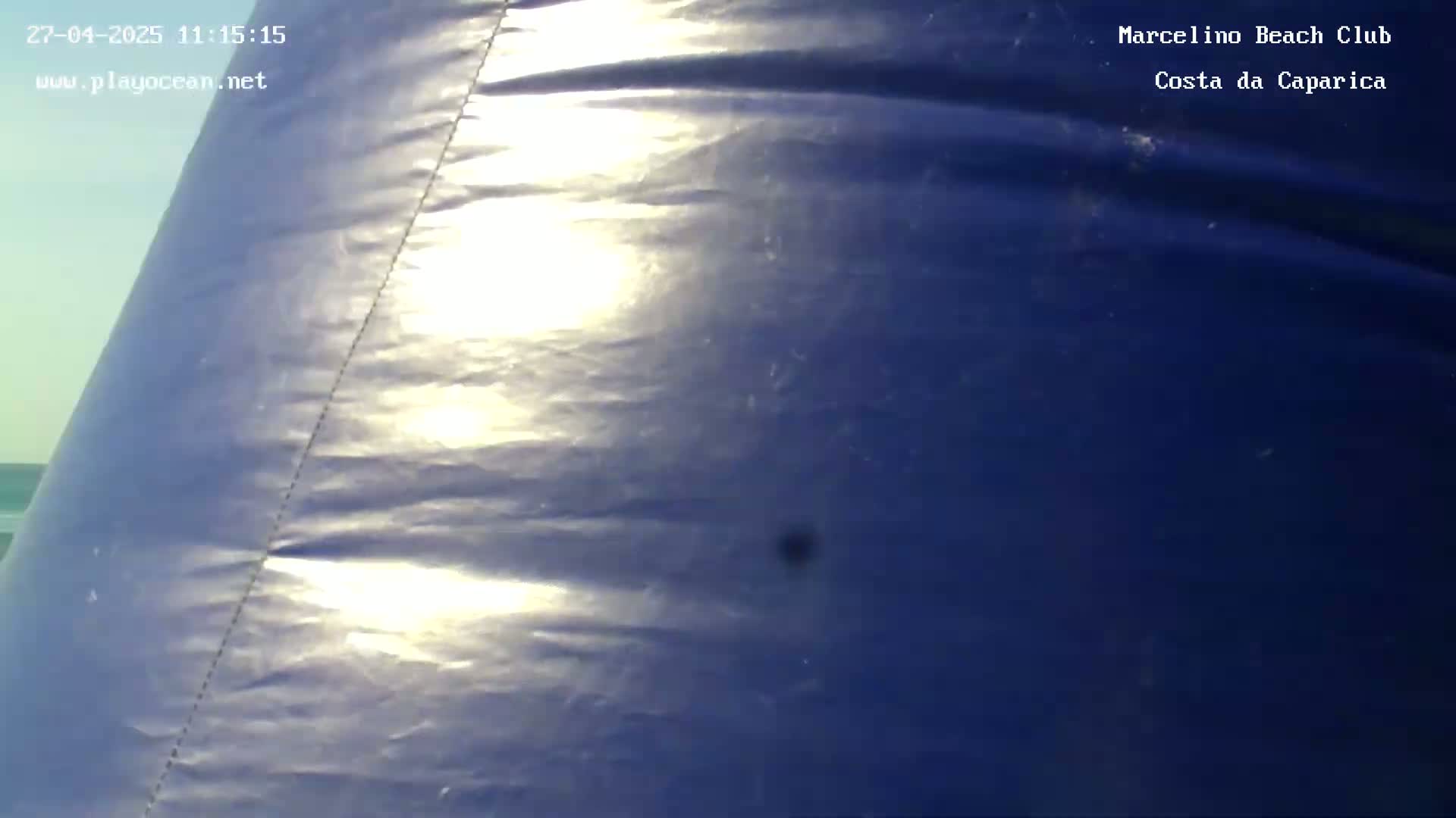 A close-up view shows a section of dark blue, seemingly inflatable material, brightly lit by sunlight in a mostly clear sky.
