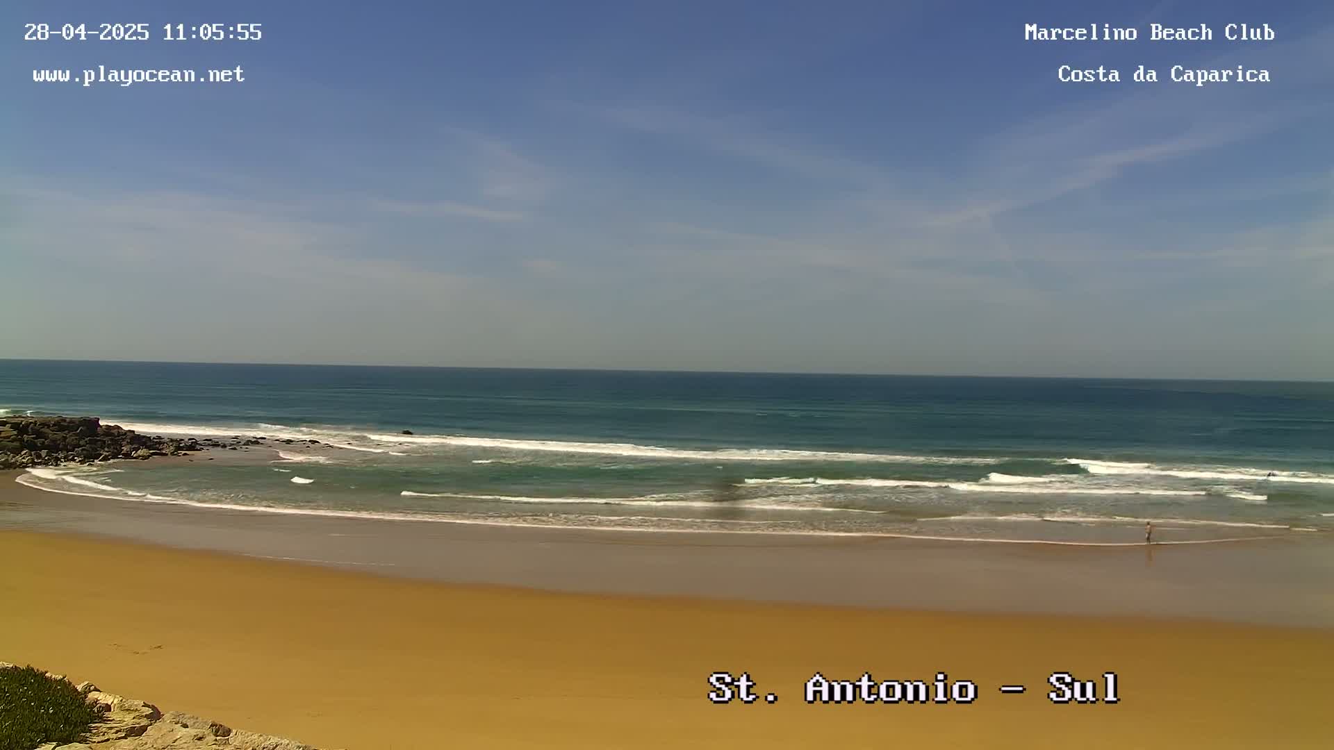 A sandy beach with gentle waves rolling onto the shore under a mostly clear sky.
