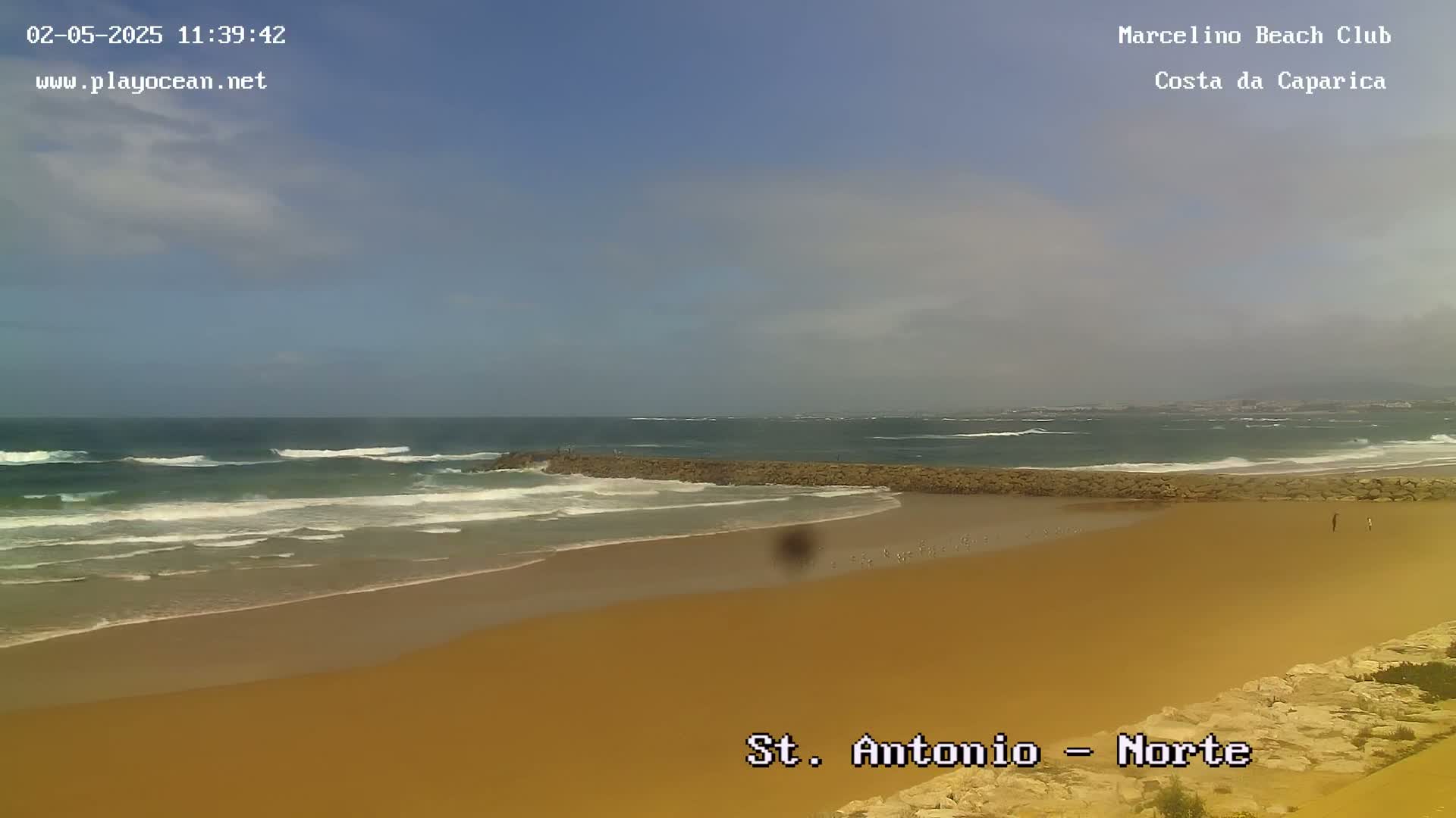 A sandy beach with moderate waves under a partly cloudy sky.