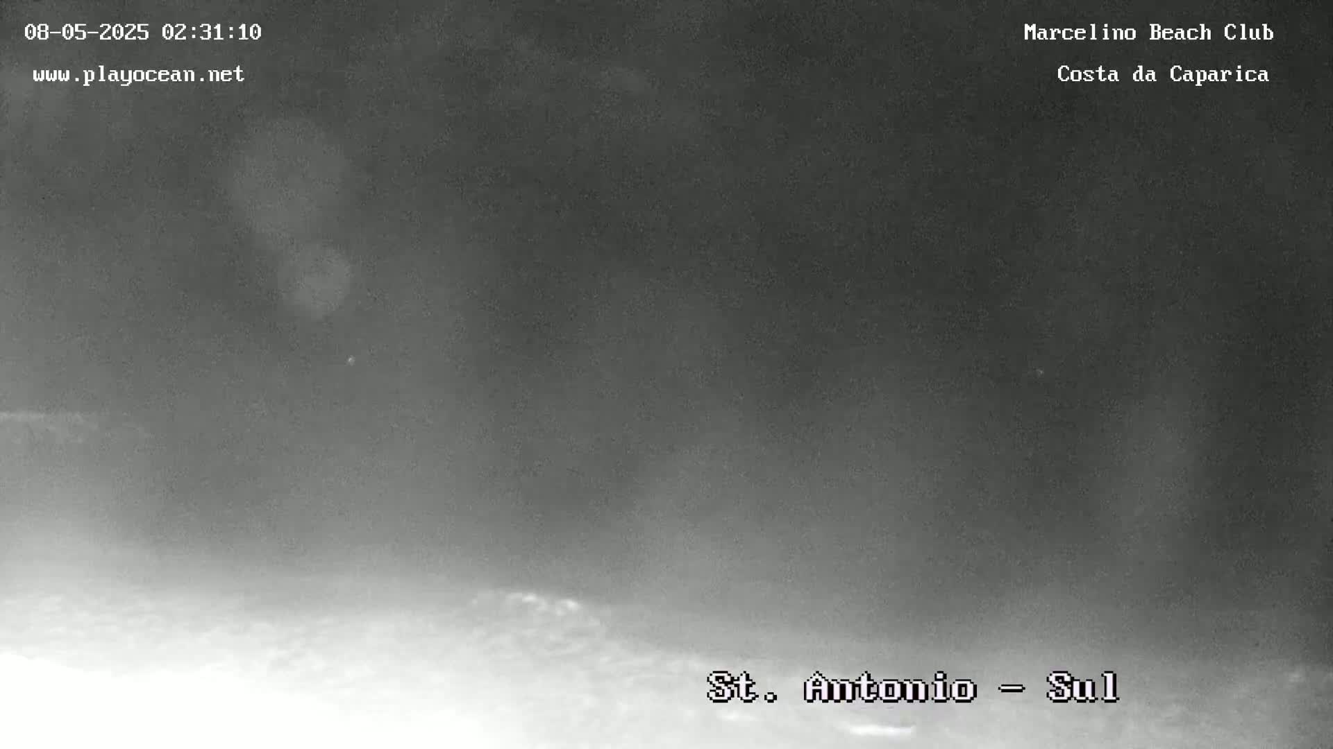 A nighttime, low-visibility view shows a dark, hazy, possibly foggy scene over what appears to be a beach or shoreline.