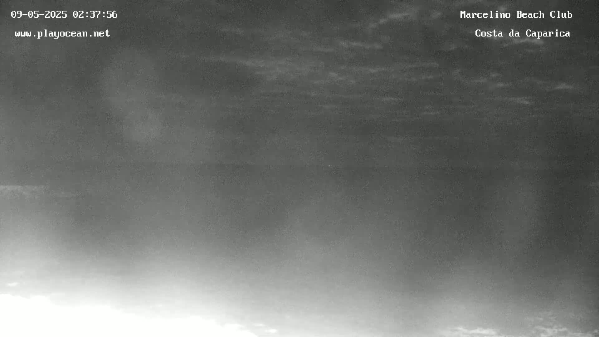 A nighttime, low-light image shows a dark, cloudy sky over a body of water.