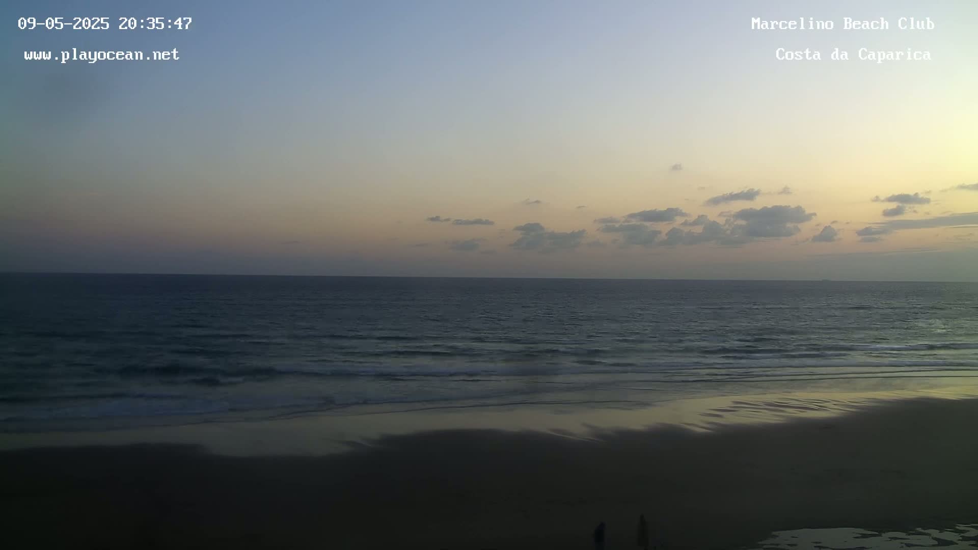 A mostly cloudy twilight sky over a dark sandy beach and gently rolling ocean.