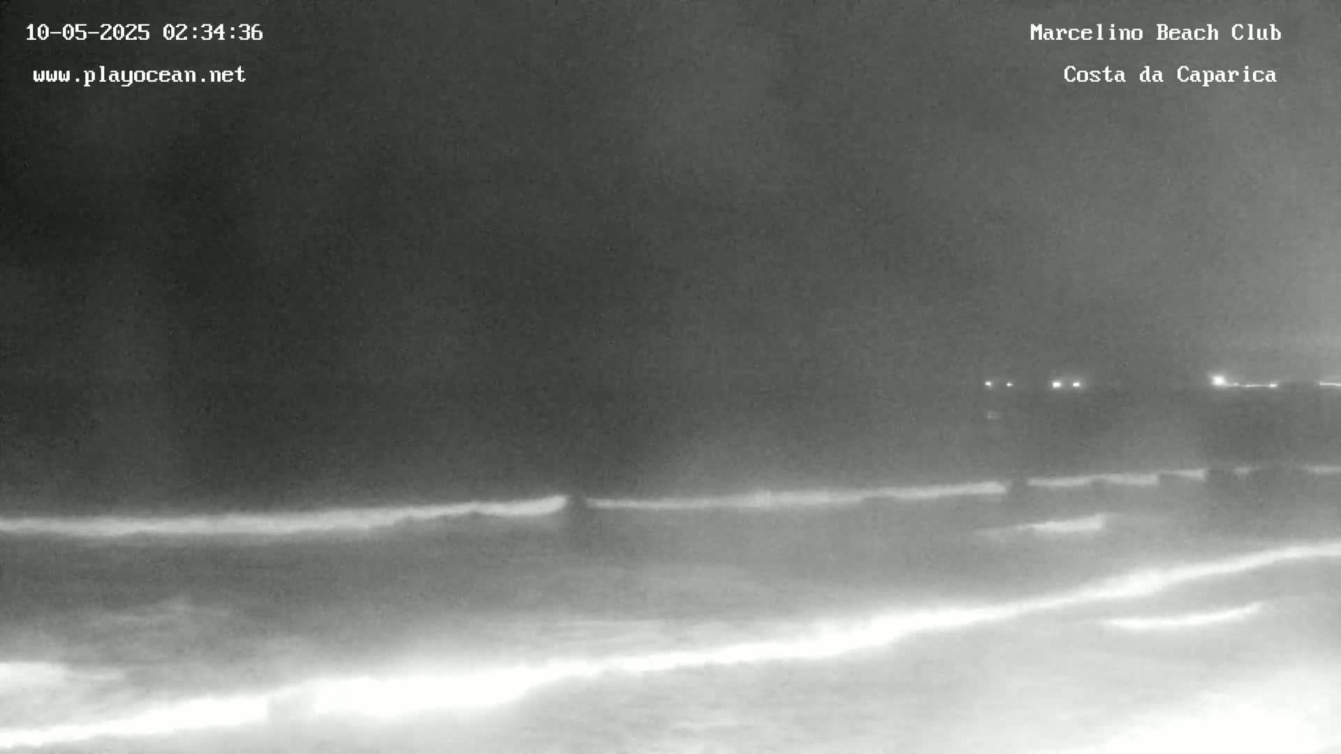 A nighttime, low-light image shows dark waves crashing on a beach under a cloudy sky.