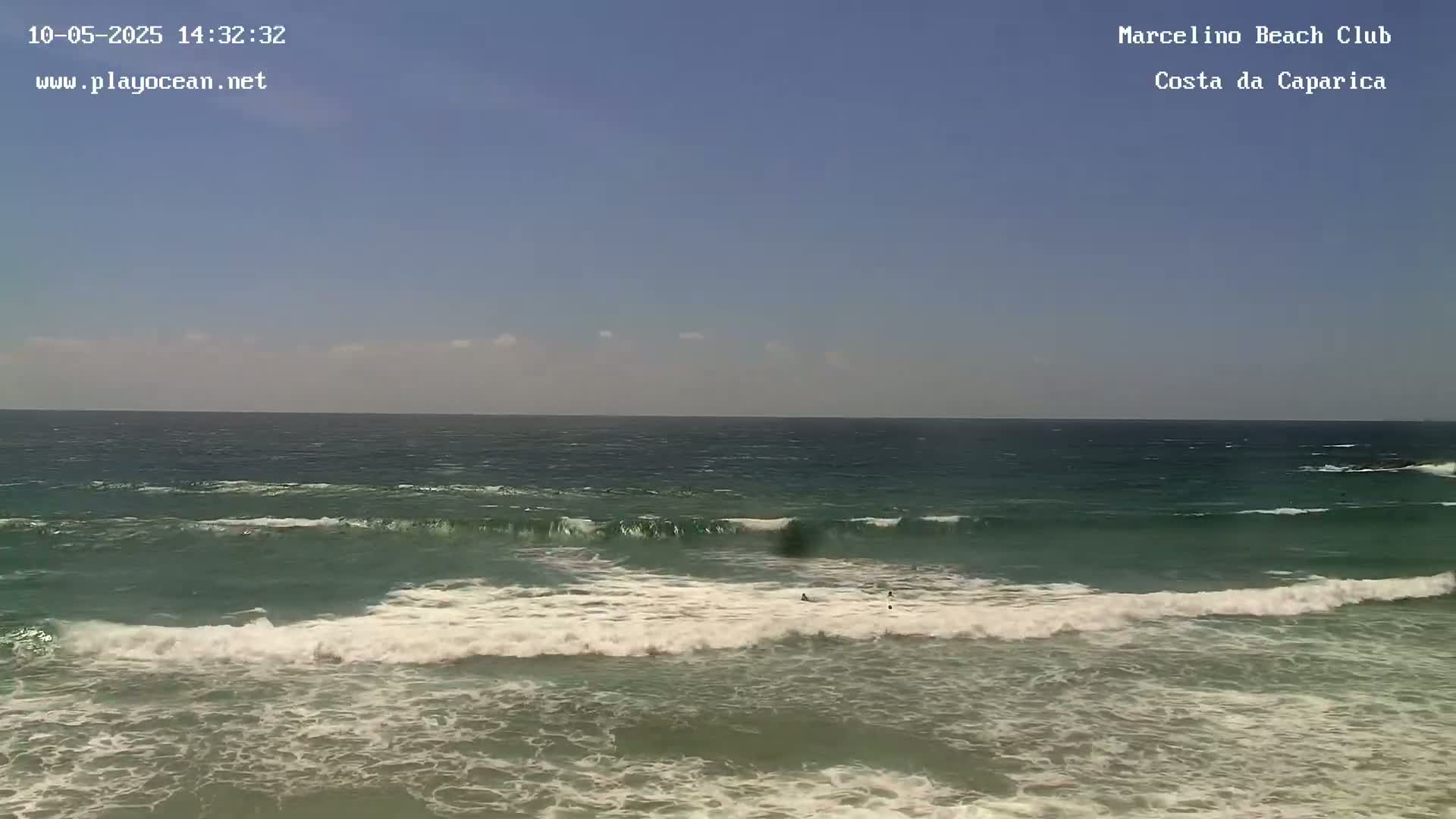Under a clear blue sky, ocean waves break onto a sandy shore.