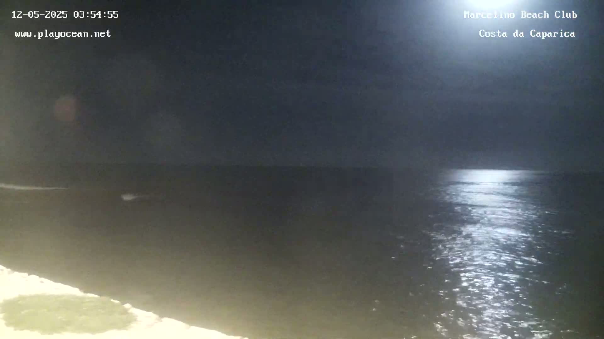 A moonlit ocean scene at night shows a dark body of water reflecting light, with a piece of land visible in the lower left corner.