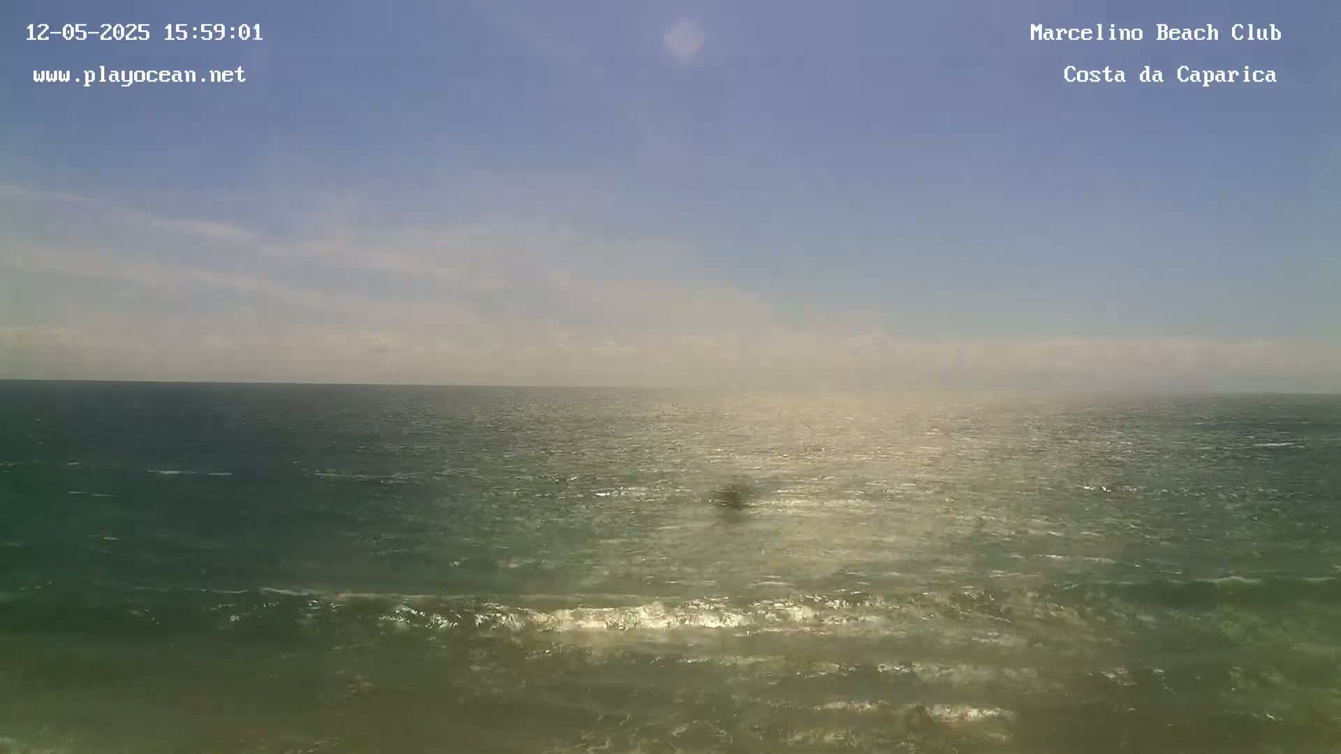 A mostly clear sky overlooks a moderately wavy ocean under sunny conditions.
