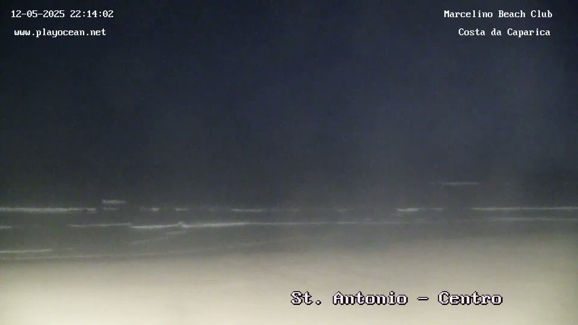 A dark nighttime beach scene shows a calm ocean with small waves gently lapping the shore.